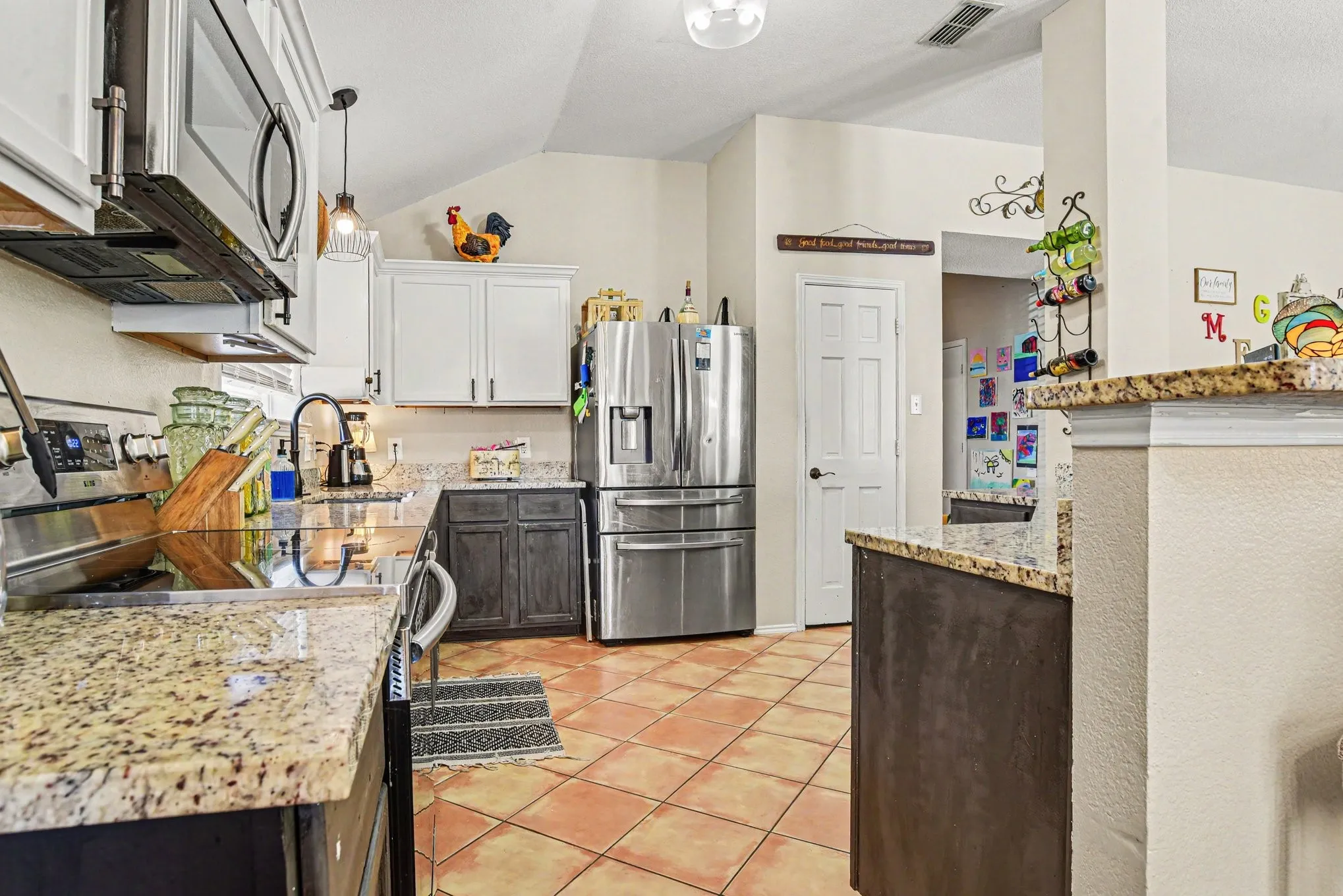 Kitchen featuring granite countertops, stainless steel appliances, ceramic tile flooring, and a vaulted ceiling