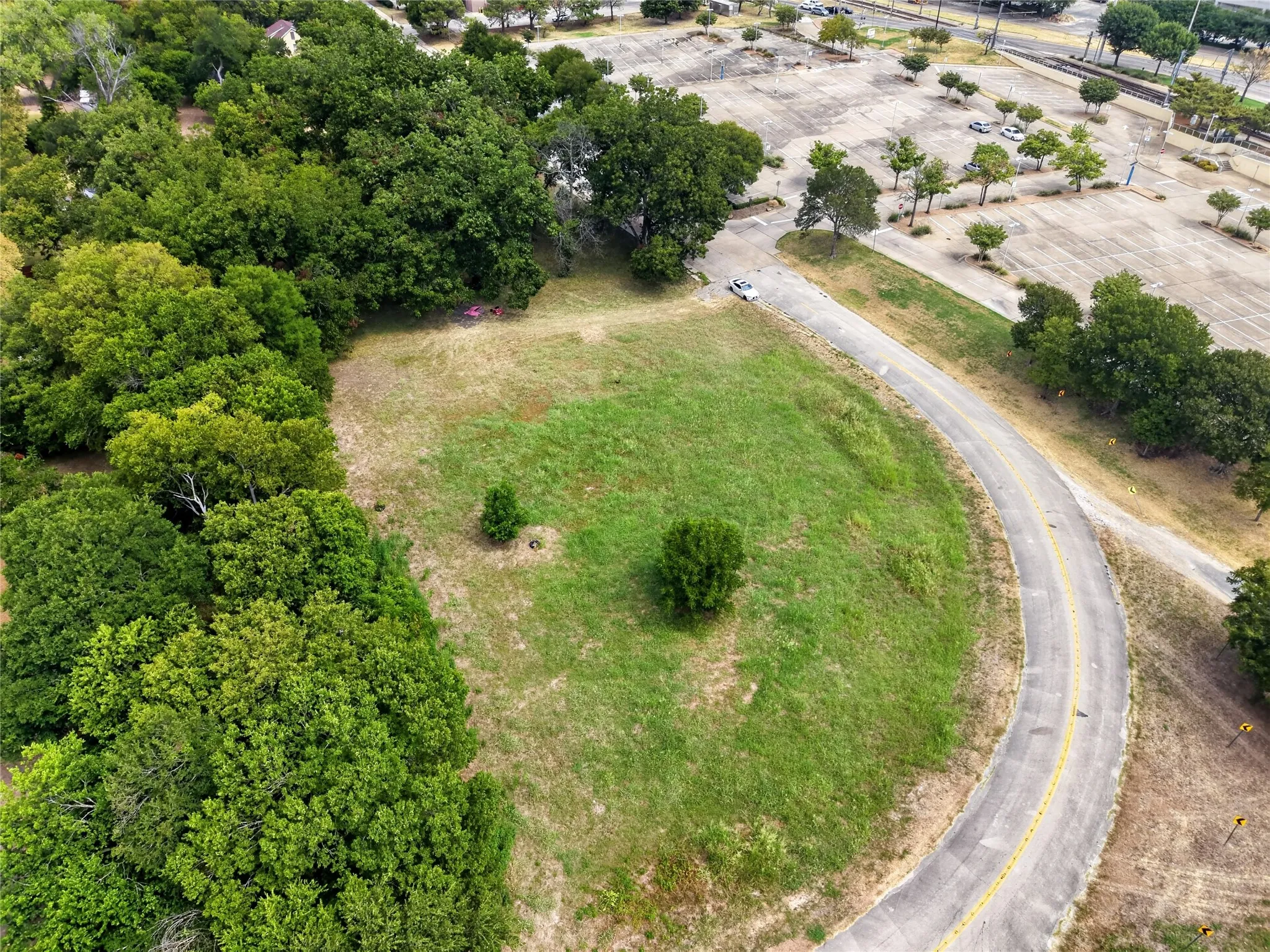Expansive lot featuring mature trees, a paved road, and adjacent undeveloped green space