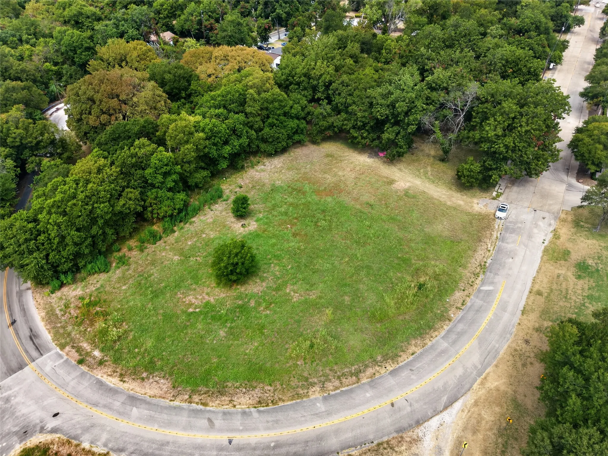 Expansive lot featuring a curvilinear paved road, lush green space, and mature perimeter trees