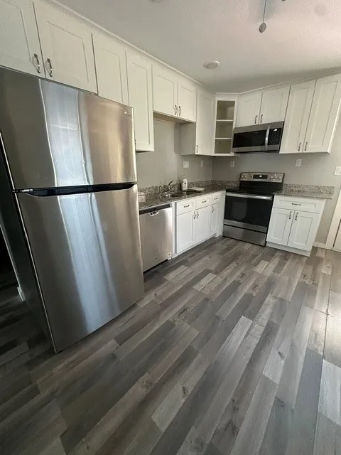 Kitchen featuring white cabinetry, light-toned countertops, stainless steel appliances, and wood-finish flooring