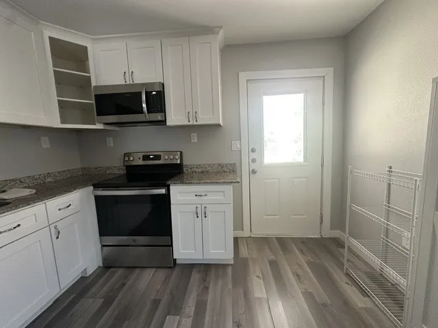 White shaker cabinetry, stainless steel appliances, granite countertops, wood-finish flooring, and a glass-paneled door