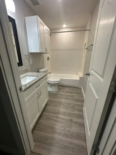 Wood-finish flooring with a white vanity featuring a granite-style countertop, undermount sink, and white cabinetry