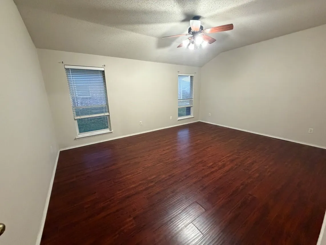 Vaulted ceiling with a ceiling fan, two windows with blinds, and wood-finish flooring