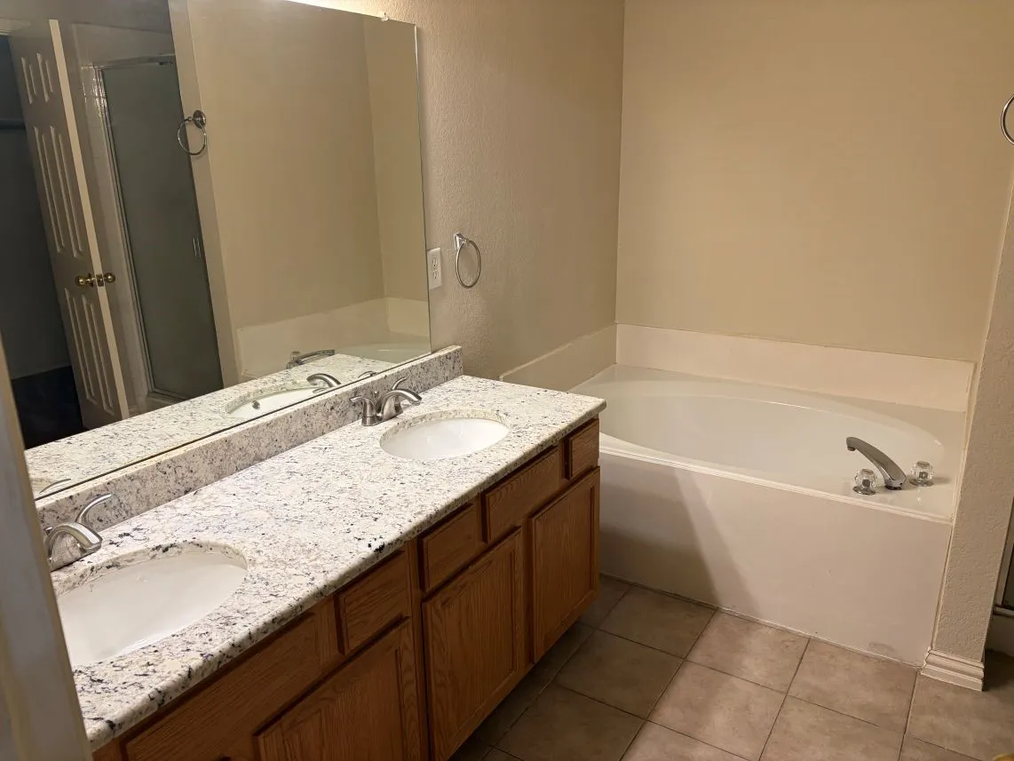 Double vanity with integrated sinks, granite countertop, wood-finish cabinetry, and a built-in soaking tub
