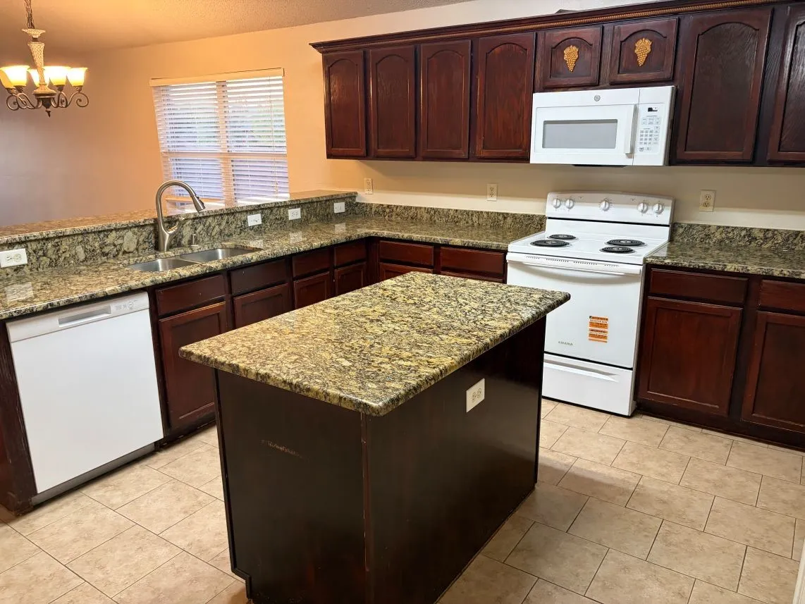 Kitchen featuring wood cabinetry, granite countertops, a center island, and tile flooring
