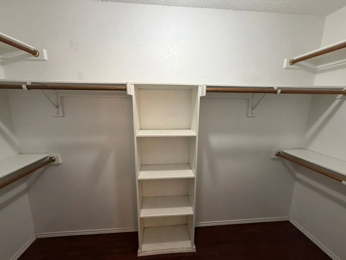 Walk-in closet with built-in shelving, multiple hanging rods, and wood-finish flooring