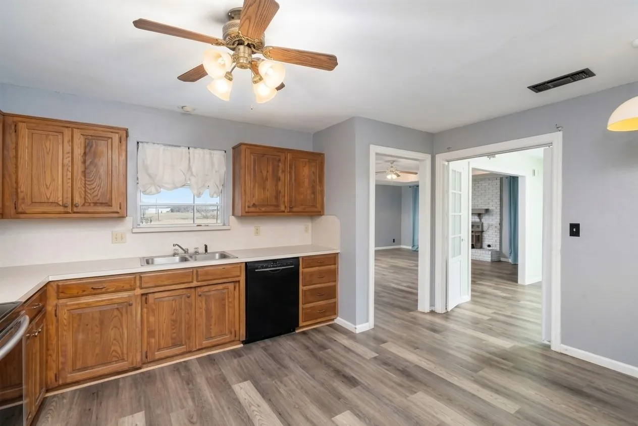 Wood-finish flooring, wood cabinetry, white countertops, stainless steel sink, and a ceiling fan with integrated lighting