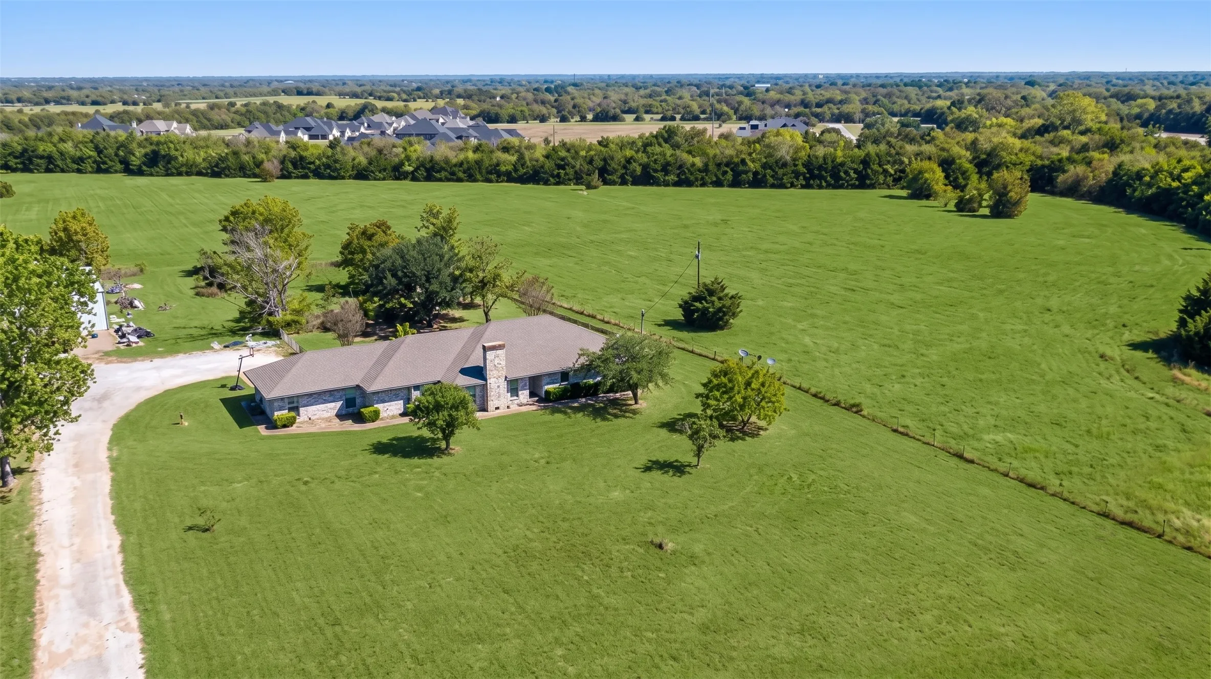 Expansive green acreage with a single-story residence, a long gravel driveway, and surrounding mature trees