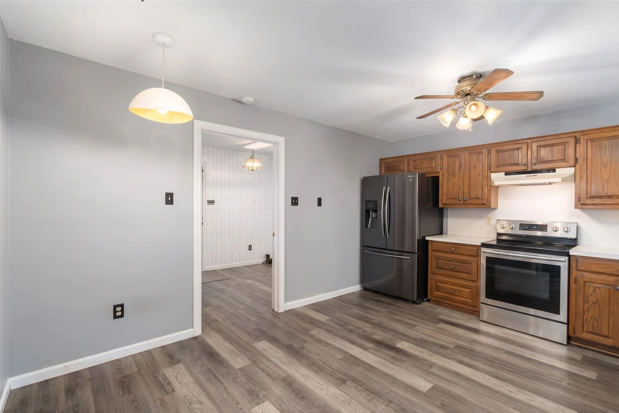 Wood-finish flooring, stainless steel appliances, wood cabinetry, white countertops, and a ceiling fan with integrated lighting