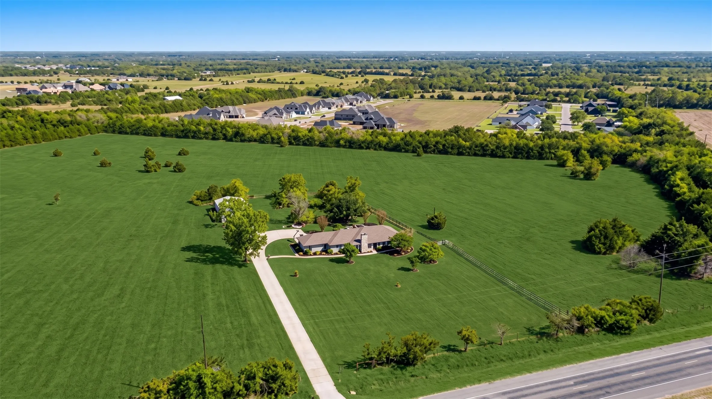 Expansive green acreage with a long paved driveway leading to a single-story residence