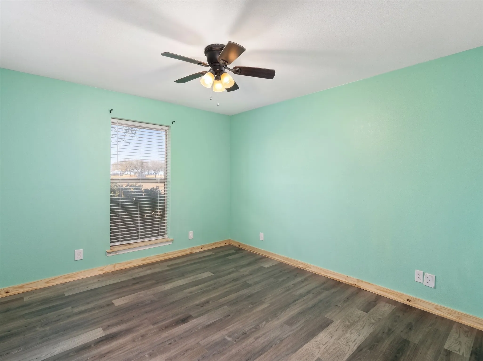 Room featuring wood-finish flooring, a ceiling fan with integrated lighting, and a window with blinds