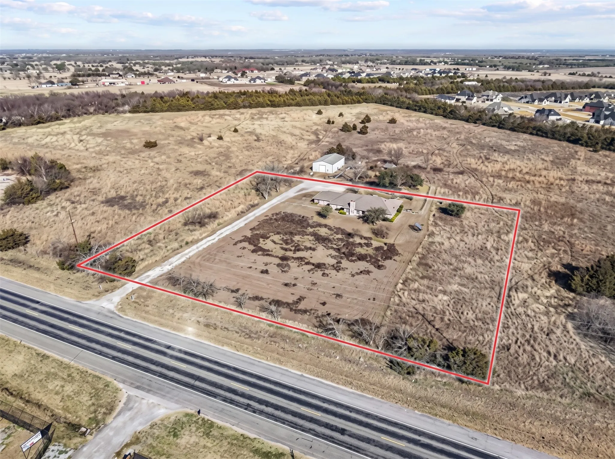 Expansive property featuring a single-story residence with a gabled roof, an auxiliary structure, and substantial open land