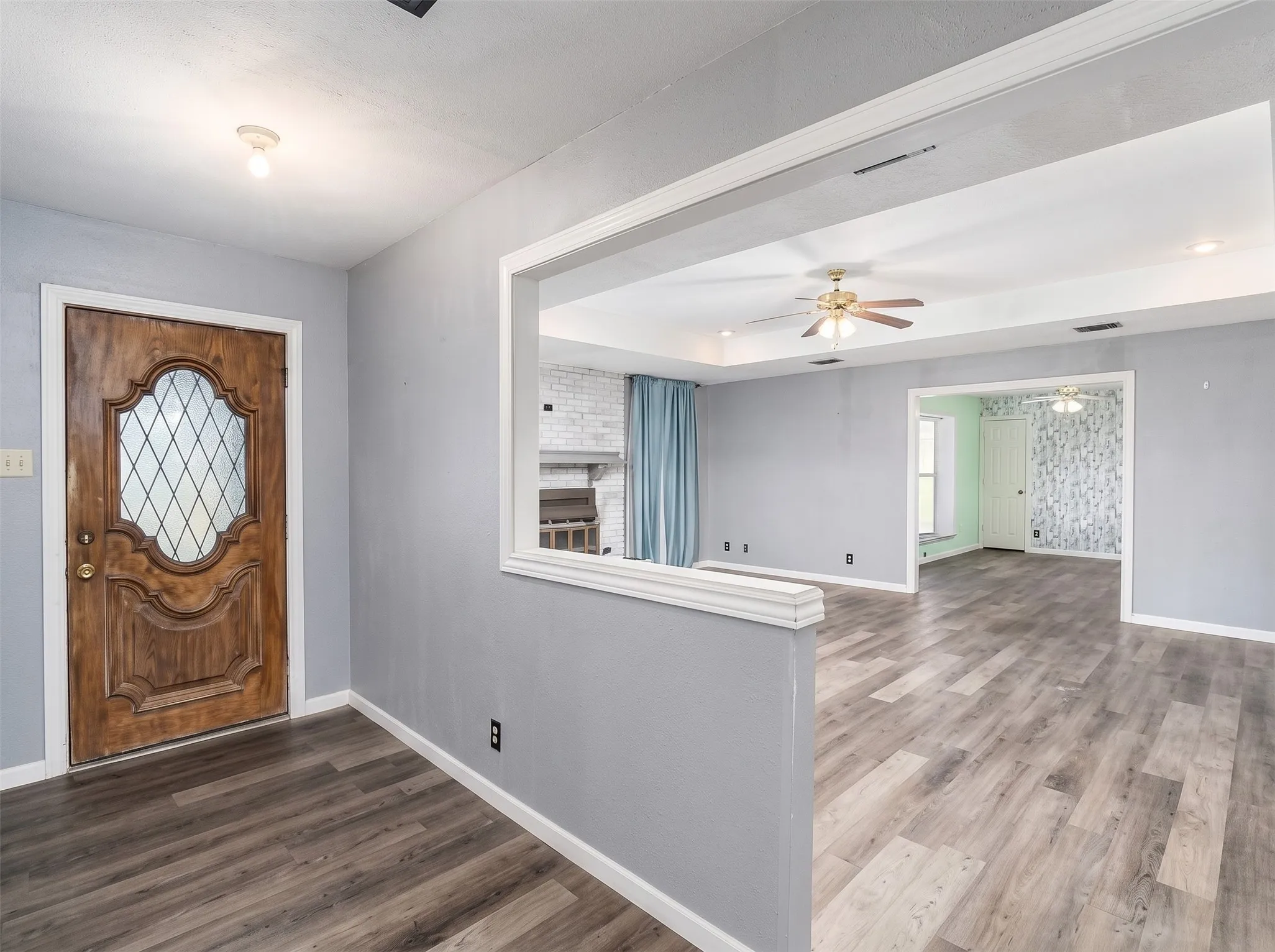 Wood-finish flooring throughout, decorative front door with leaded glass, recessed ceiling with fan, and a fireplace with a white brick surround