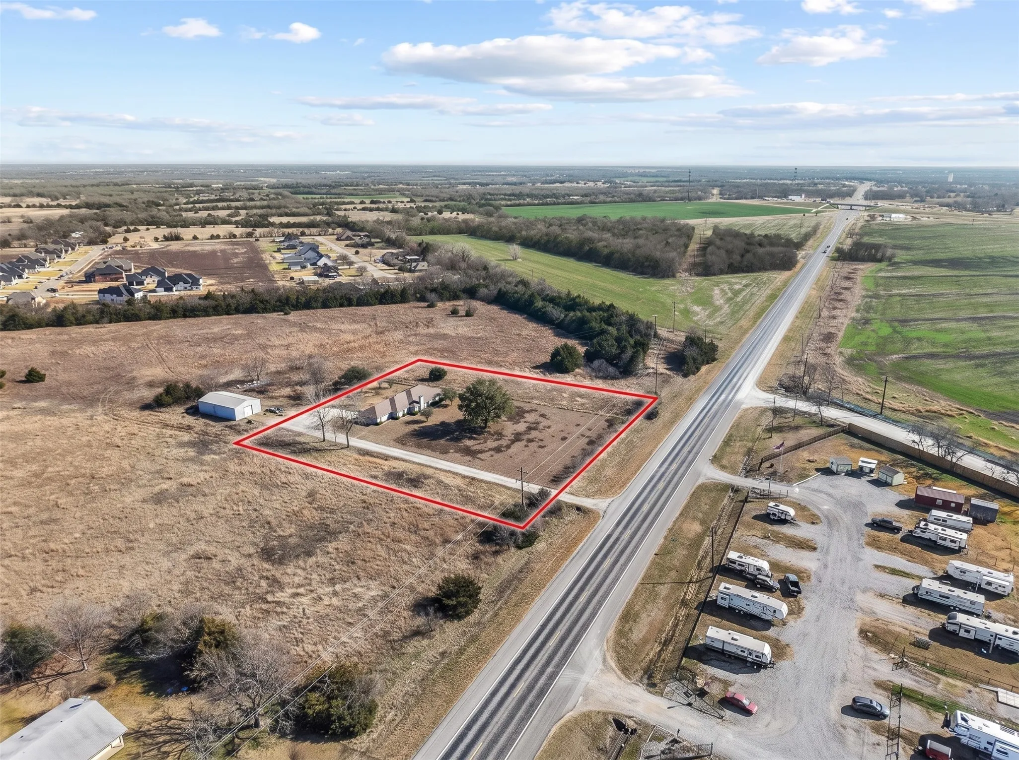 Expansive undeveloped lot with highway access, featuring a primary residence, two smaller structures, and a separate outbuilding