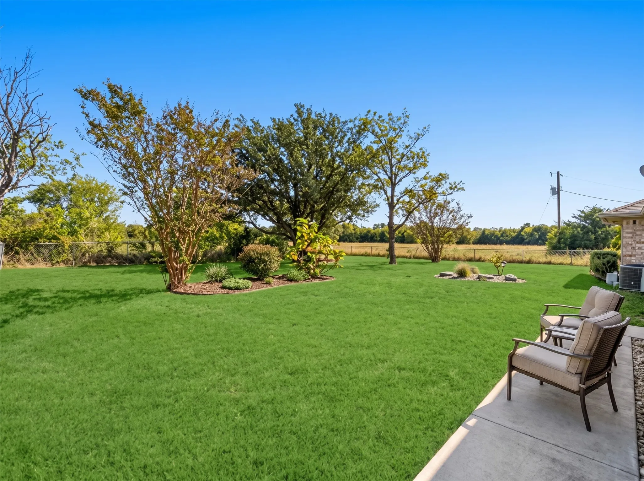 Expansive backyard with a lush lawn, mature trees, and a concrete patio