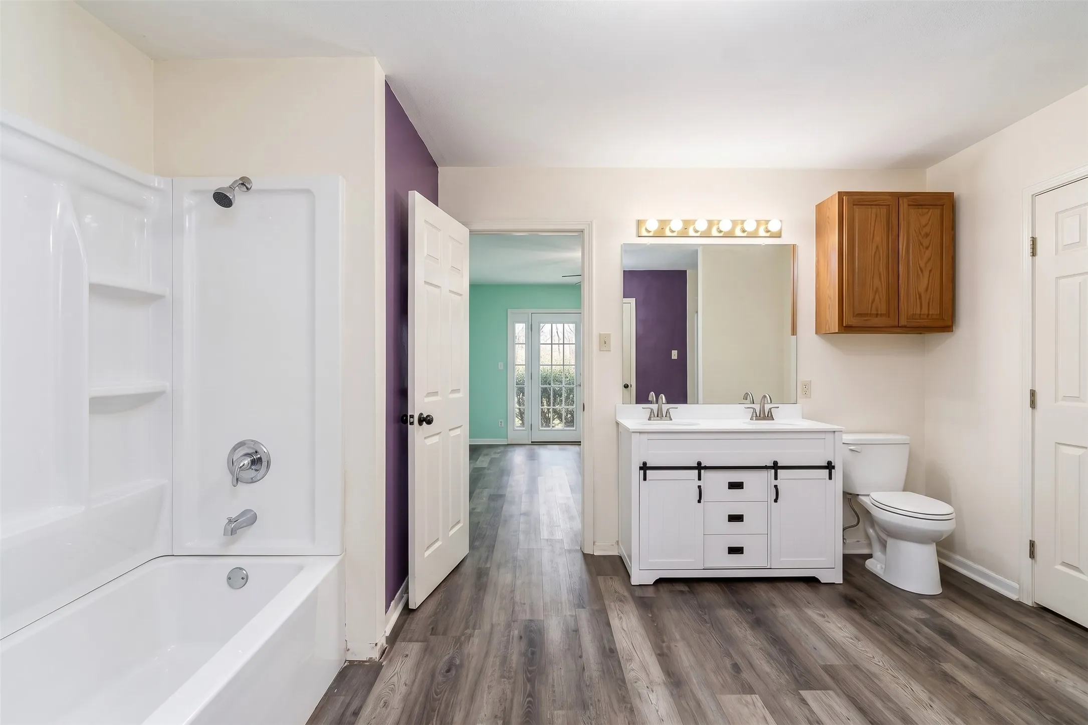 White double vanity with dual vessel sinks, barn-door style cabinetry, wood-finish flooring, and a white integrated tub and shower unit