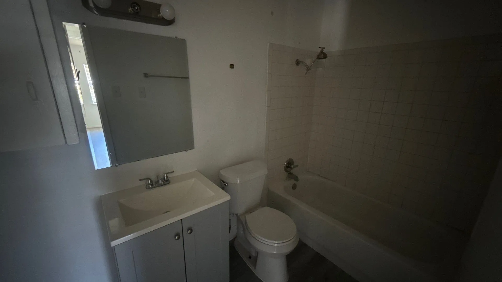White bathtub with subway tile surround, vanity with integrated sink, chrome faucet, and mirrored medicine cabinet