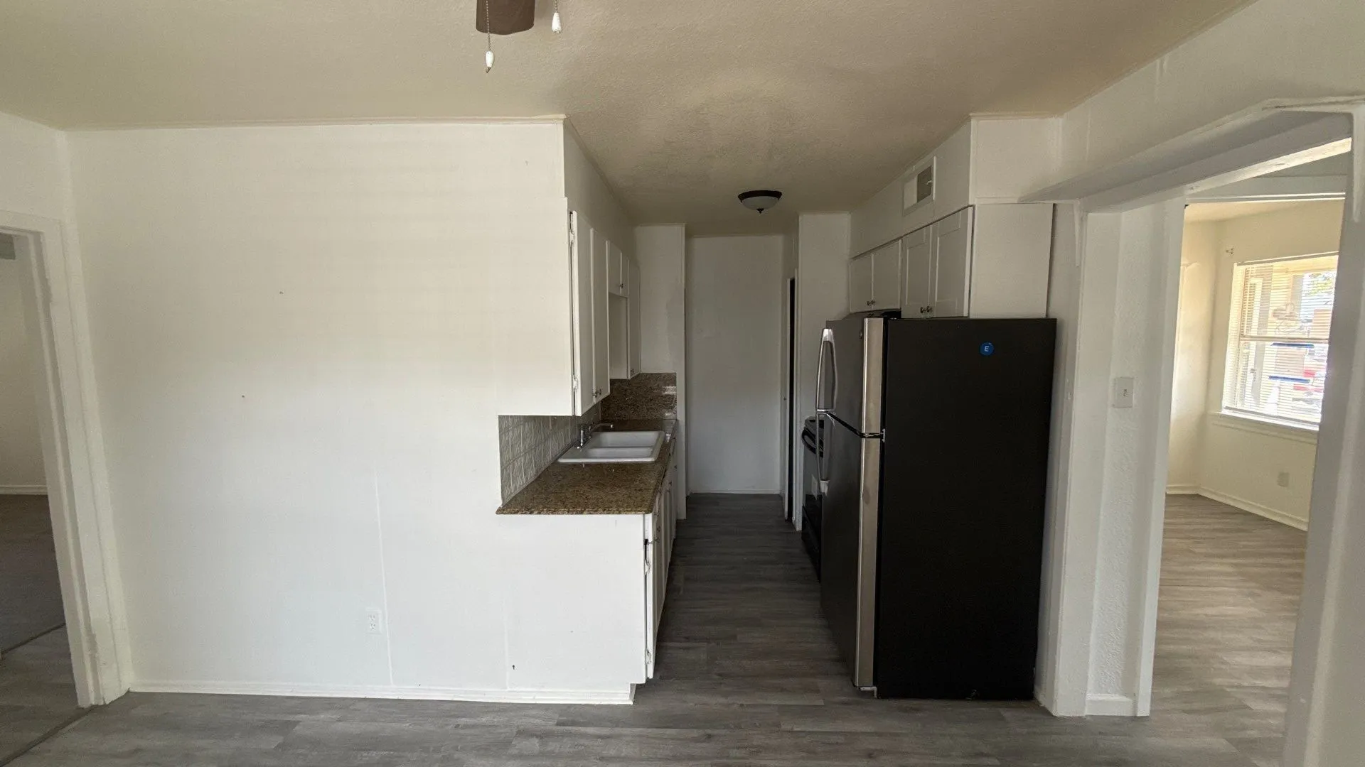 Kitchen featuring wood-finish flooring, white cabinetry, a double basin sink, and integrated black appliances
