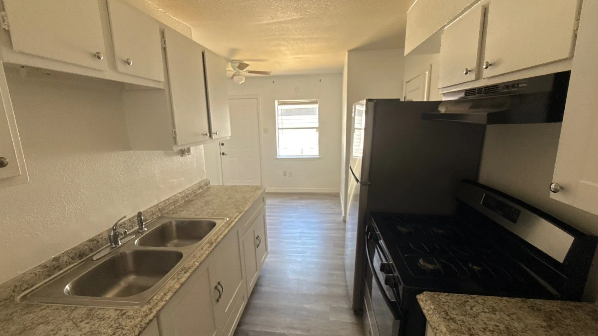 Galley kitchen featuring white cabinetry, dual basin sink, black range, and refrigerator