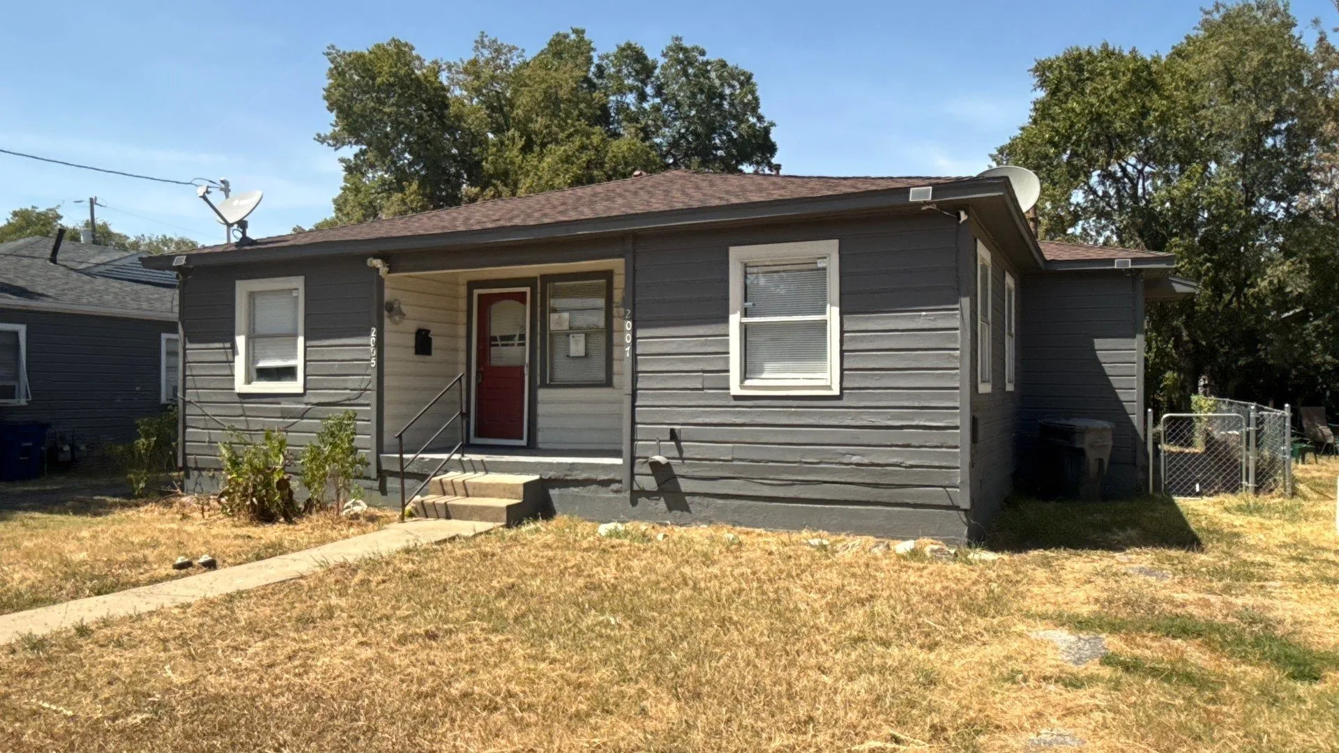 Gray horizontal siding exterior with a dark brown shingle roof, featuring a covered front porch with a red entry door and white trim