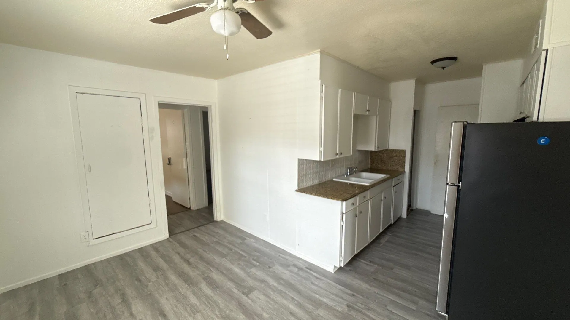 Wood-finish flooring throughout, white cabinetry, double basin sink, white tile backsplash, and a ceiling fan with light fixture
