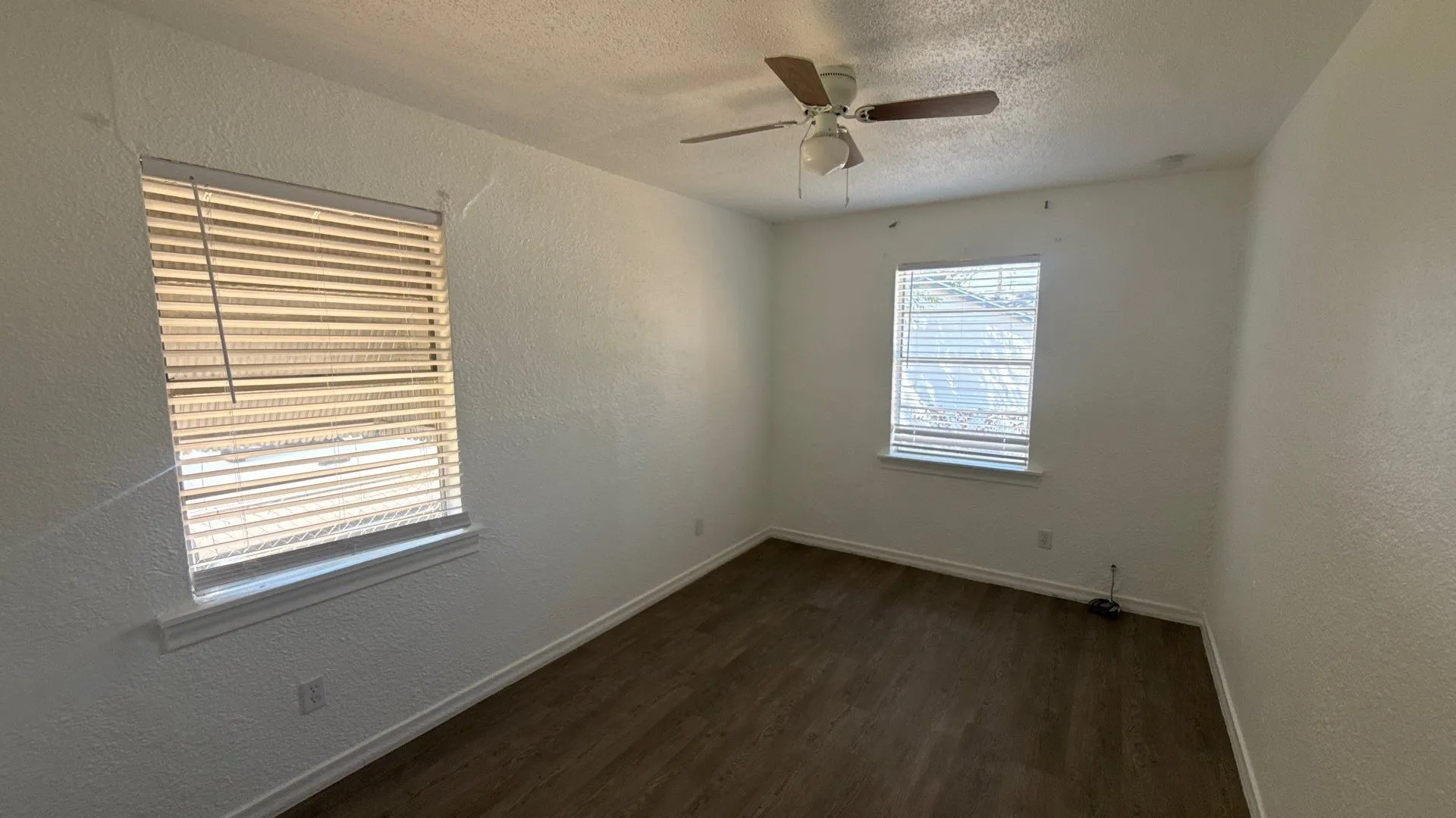 Wood-finish flooring, two windows with blinds, a ceiling fan with light, and white painted walls