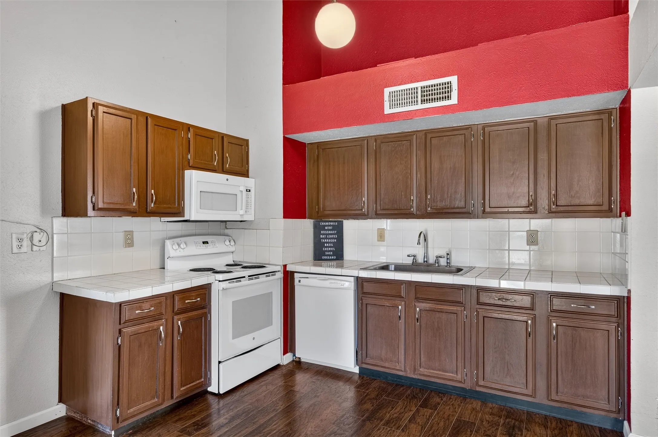 Wood-finish flooring, white tile backsplash, full-height cabinetry, white appliances, and a stainless steel sink with a high-arch faucet