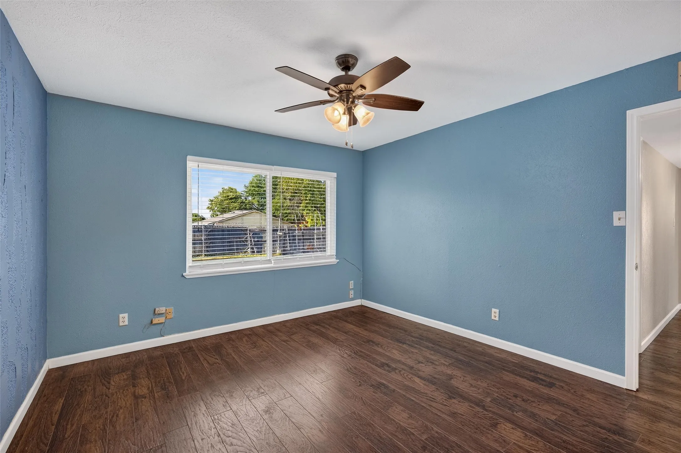 Wood-finish flooring, ceiling fan with integrated lighting, window with blinds, and blue painted walls