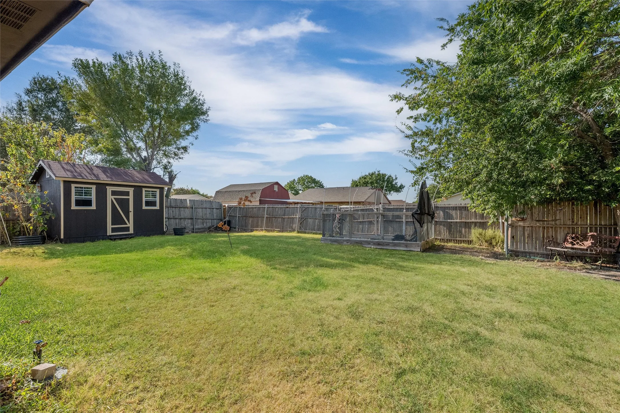 Expansive backyard featuring a manicured lawn, wood-paneled privacy fence, and a dark-toned storage shed with white trim