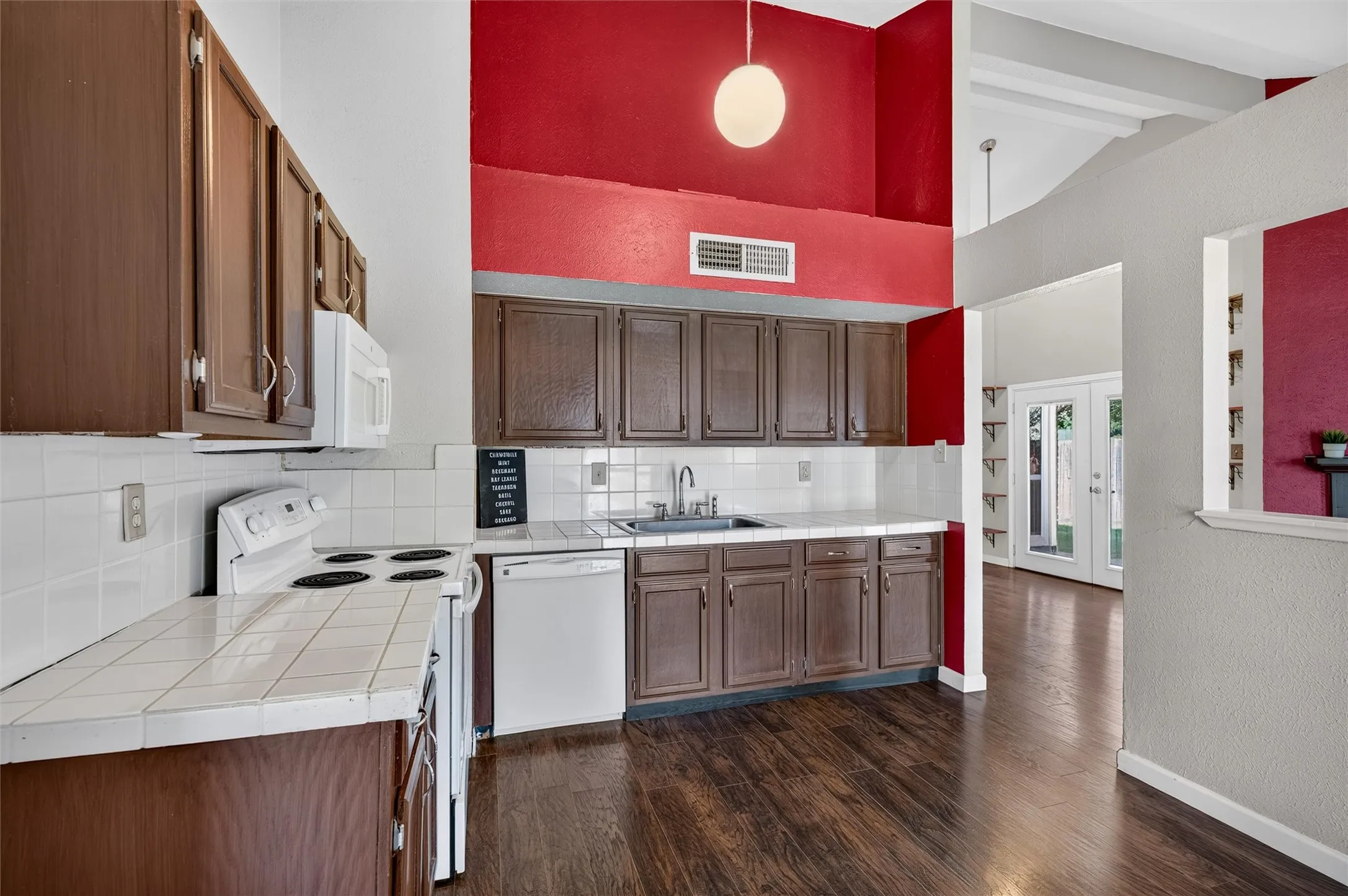 Kitchen featuring wood-finish flooring, white tile countertops, white tile backsplash, and dark wood cabinetry