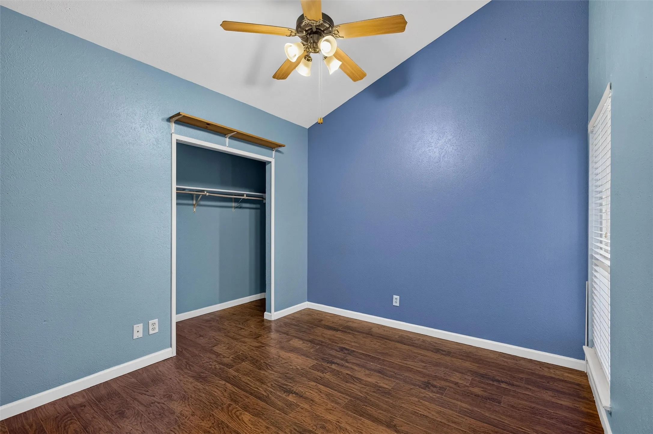 Vaulted ceiling with a ceiling fan, wood-finish flooring, built-in closet, and vertical window blinds