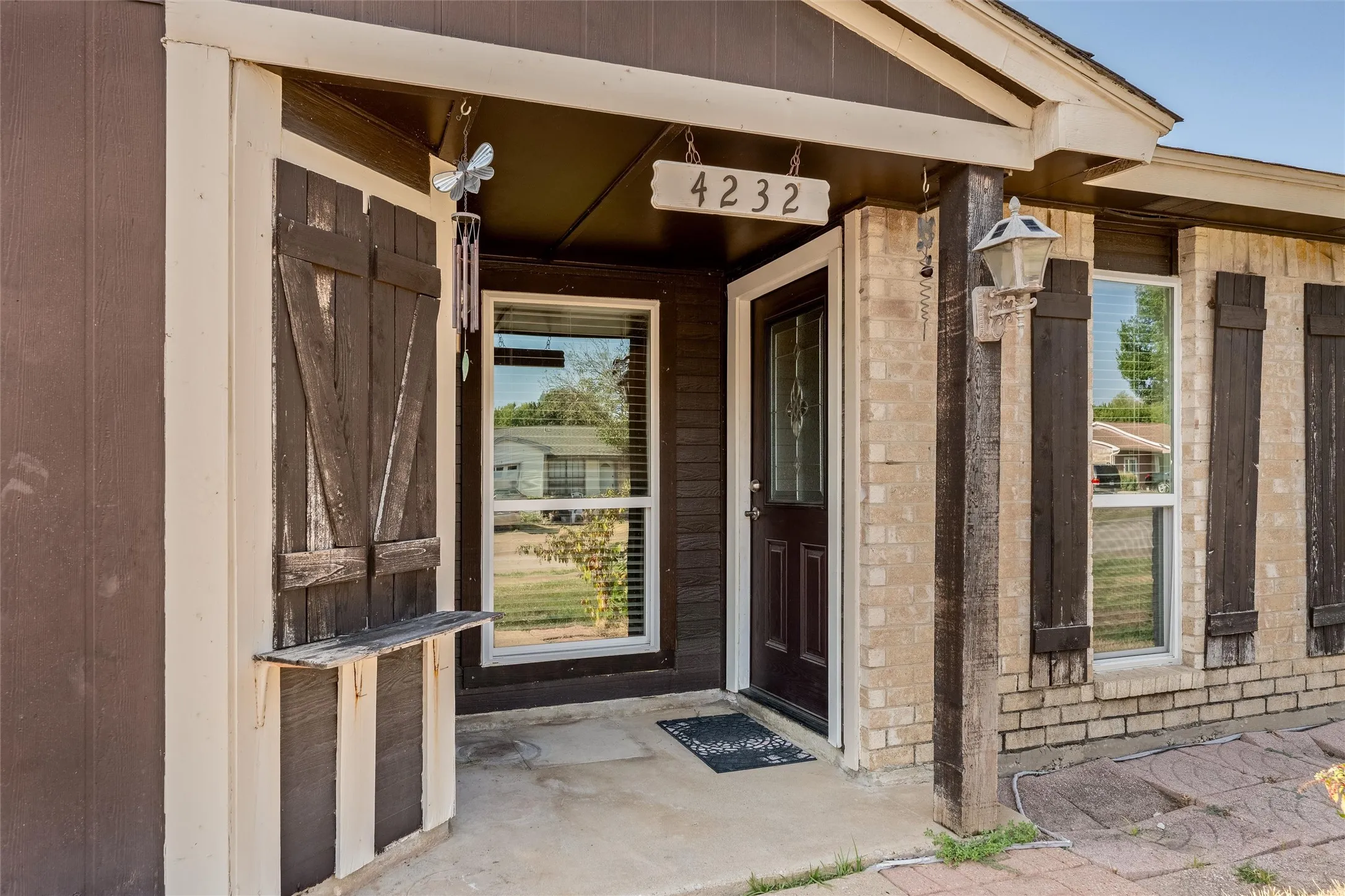 Front entry featuring a panel door with decorative glass, two windows with blinds, and brick siding