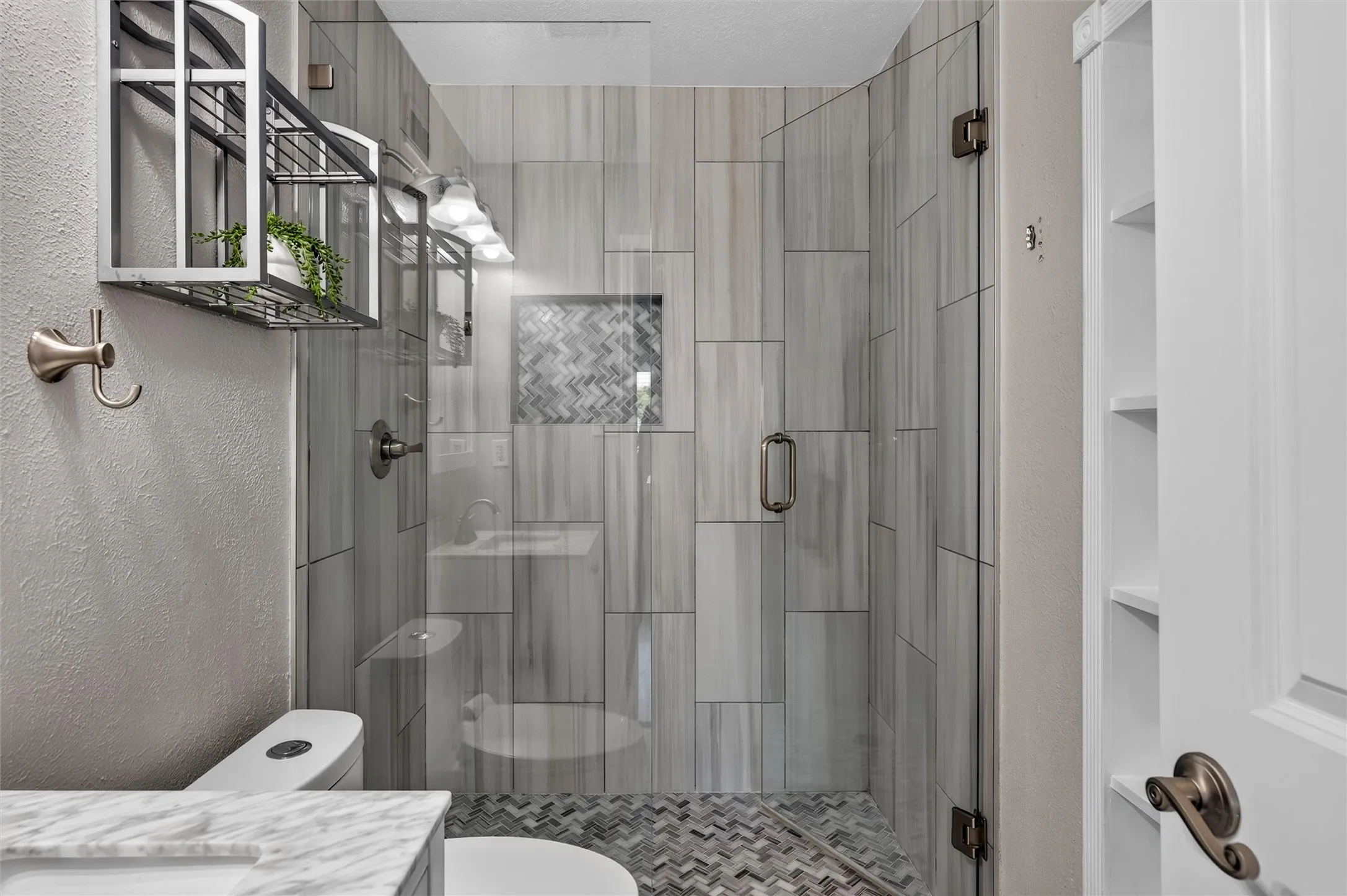 Glass-enclosed shower with vertical tile and a herringbone-patterned floor
