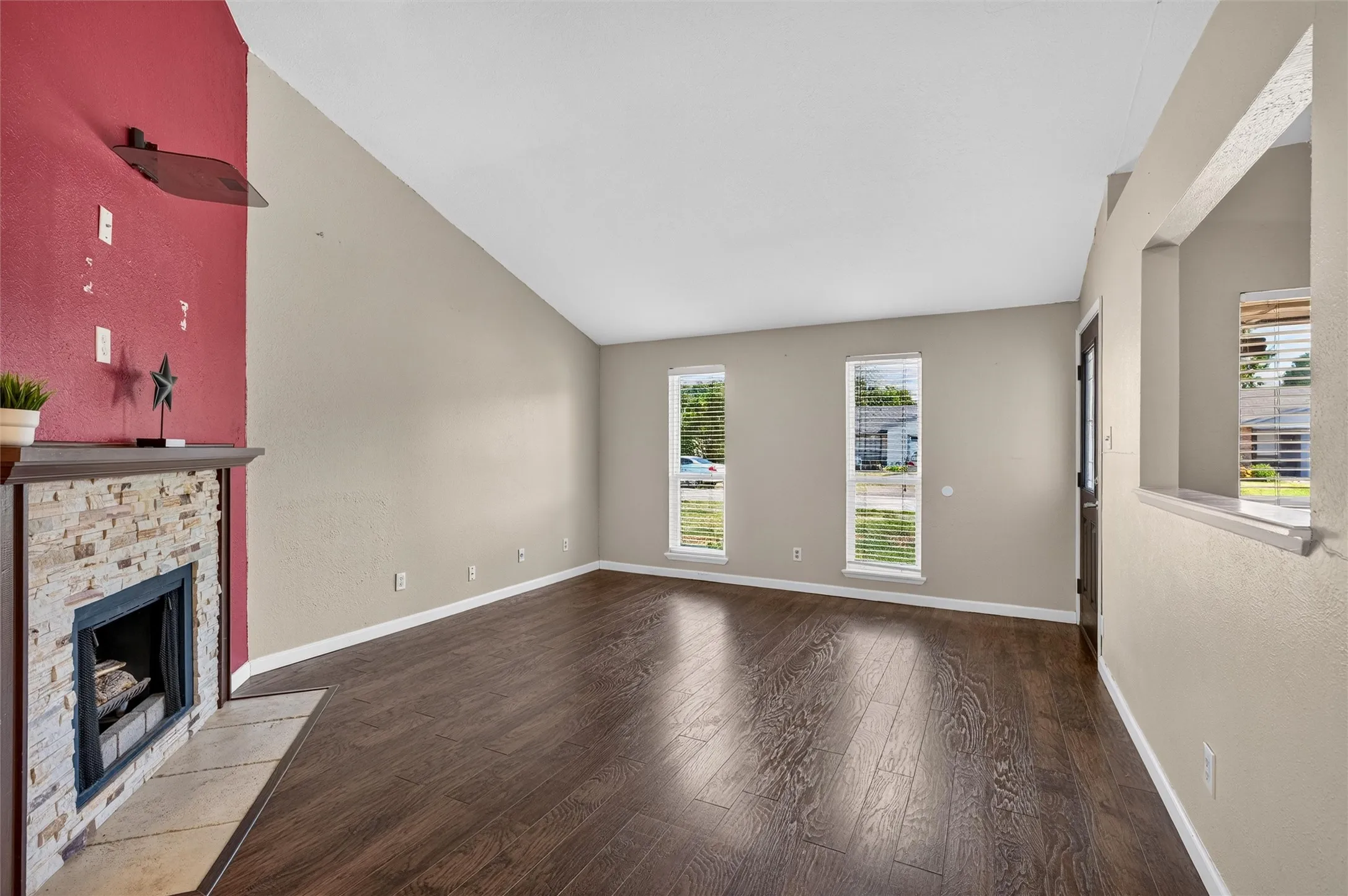 Spacious living area featuring a vaulted ceiling, wood-finish flooring, and a stone-front fireplace with a wood mantel