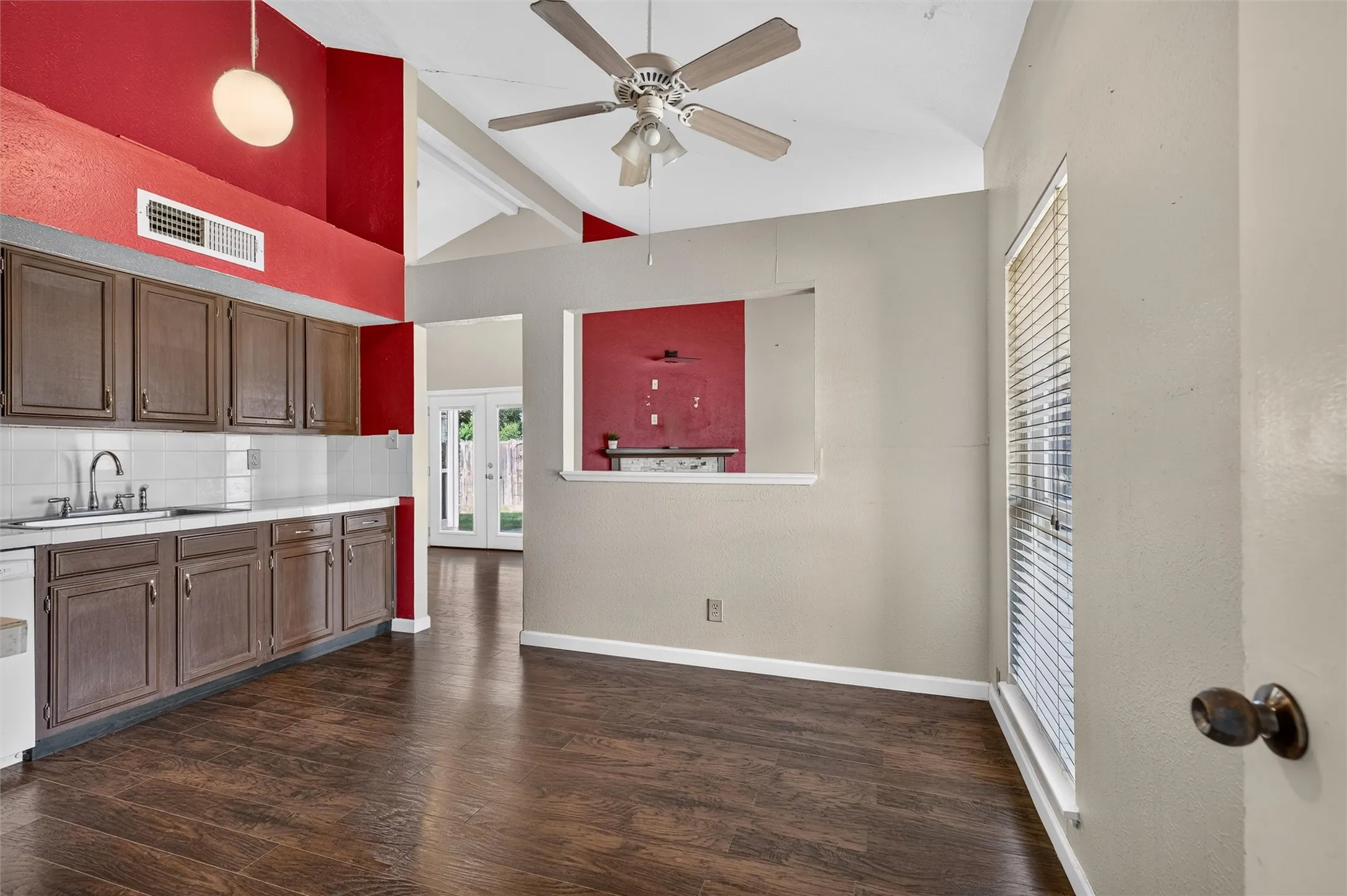 Vaulted ceiling with a ceiling fan, wood-finish flooring, built-in cabinetry, and a kitchen pass-through