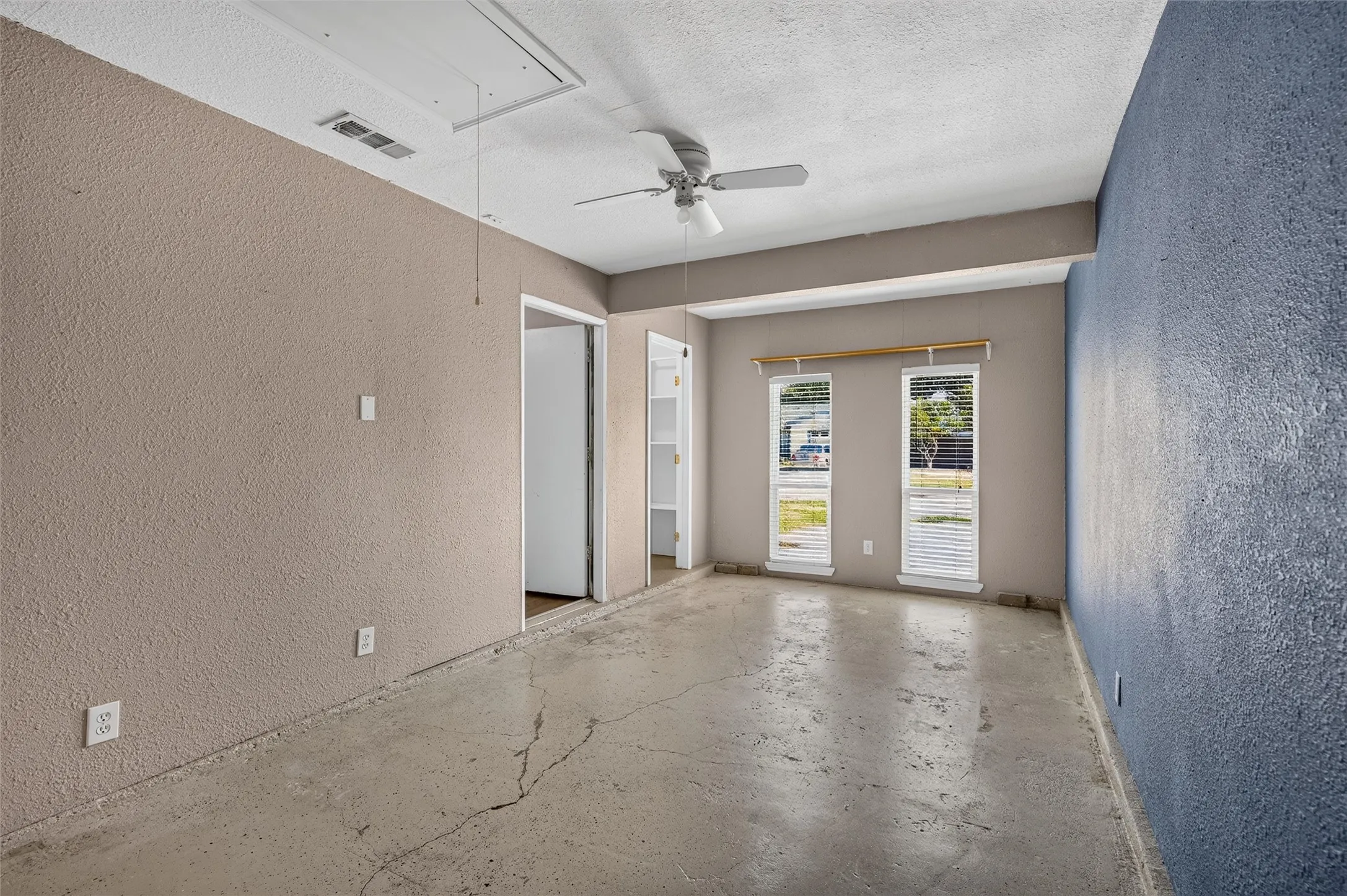 Ceiling fan with light kit, textured walls with dual-tone paint, two windows with blinds, and exposed concrete flooring