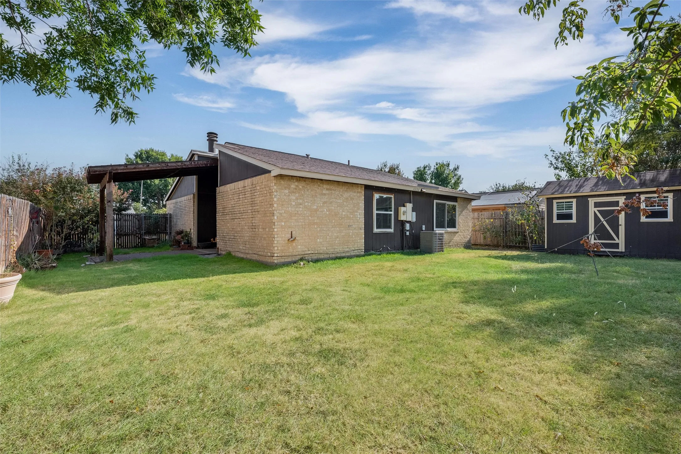 Expansive backyard featuring a manicured lawn, a detached storage shed, and a covered patio area