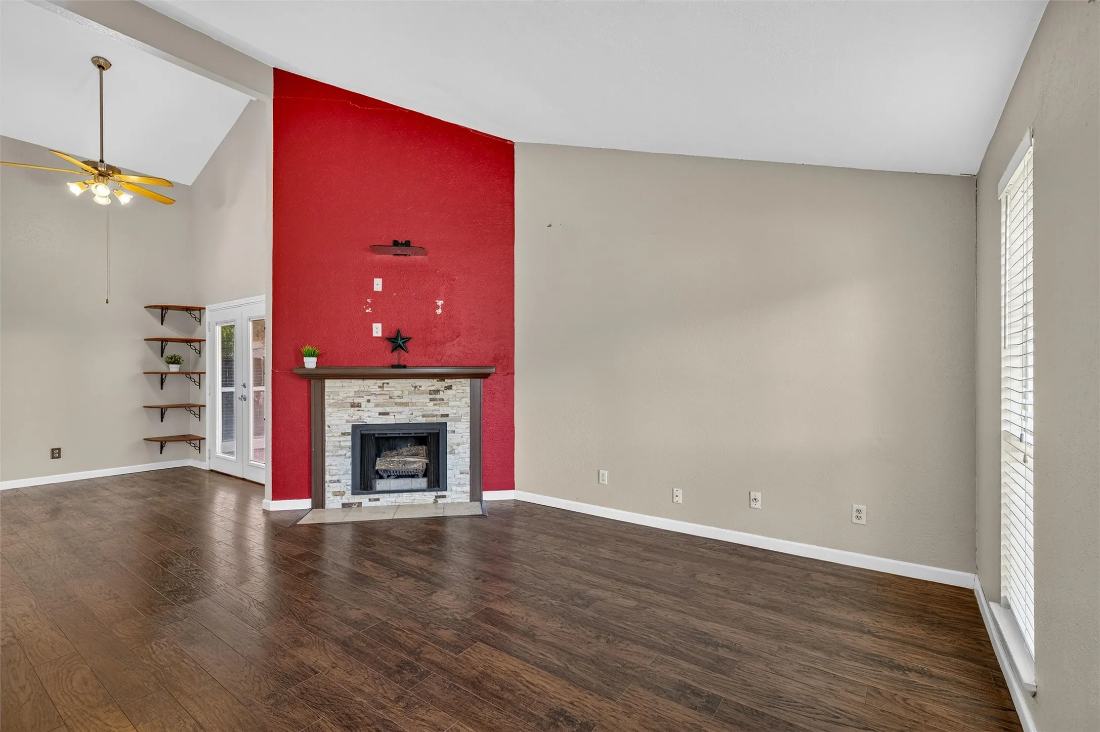 Vaulted ceiling with an attached ceiling fan, wood-finish flooring, stone-faced fireplace, and built-in wood shelving