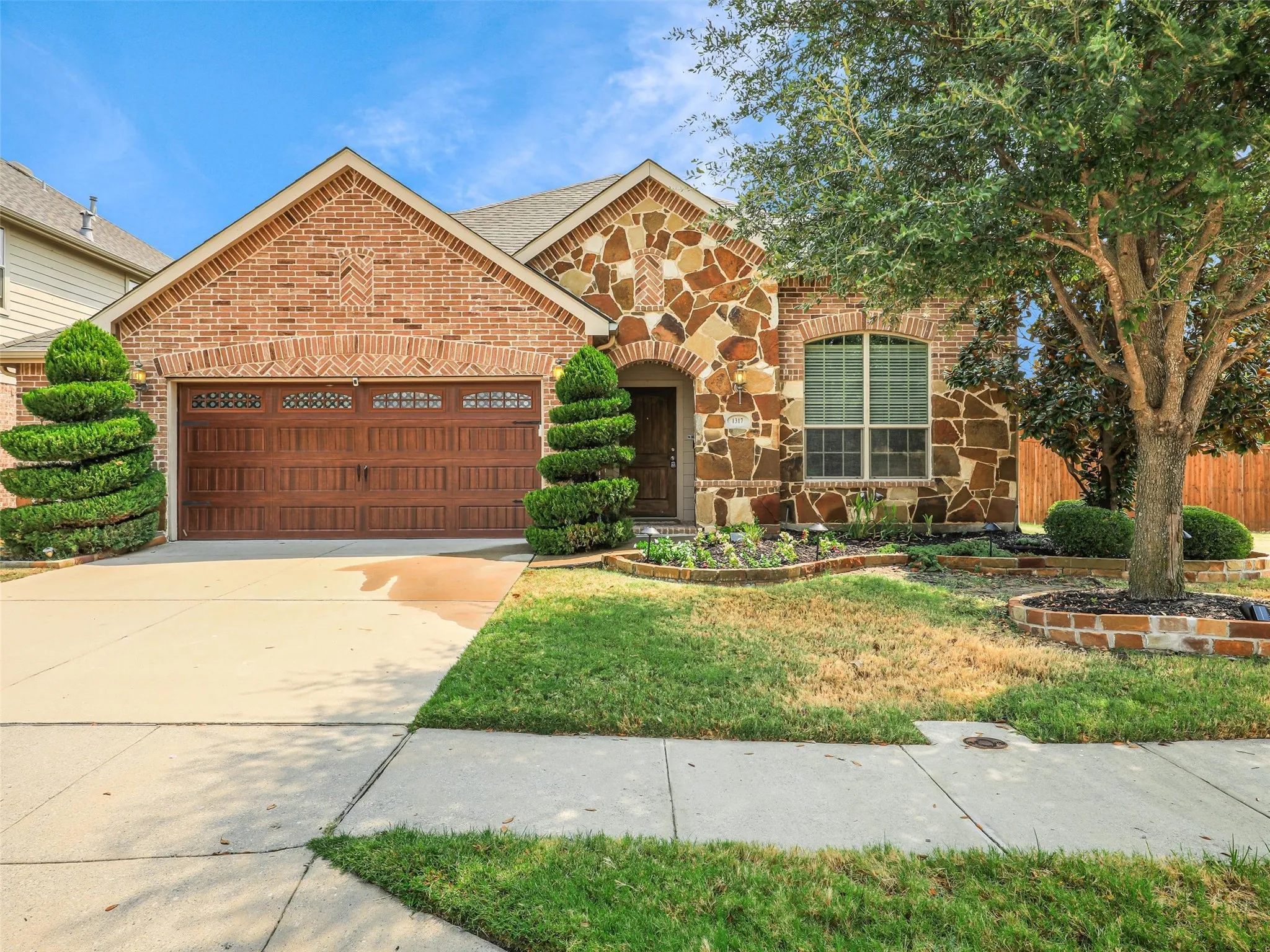 Welcoming single-story exterior with attractive brick-and-stone accents, mature trees, and neatly maintained landscaping.