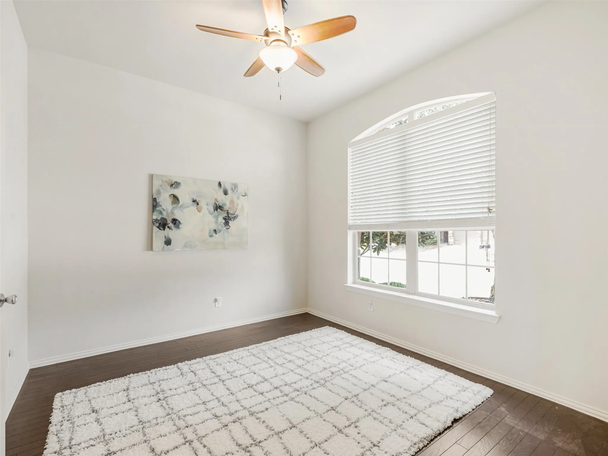 Dining room with wood flooring, a ceiling fan, and a large arched window that fills the space with natural light.