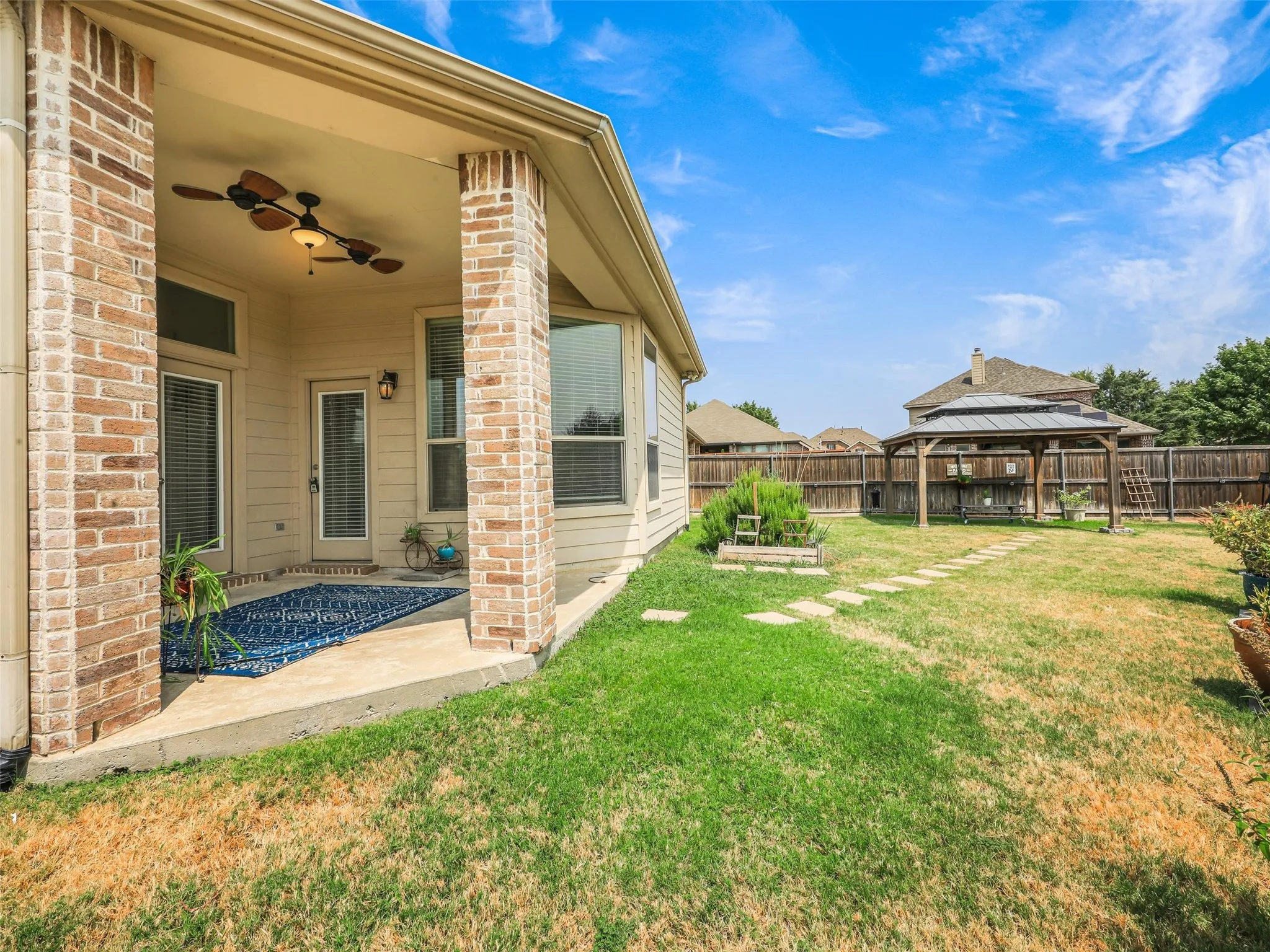 Spacious fenced backyard features a covered patio, garden beds, stepping-stone pathways, and multiple areas for outdoor enjoyment.