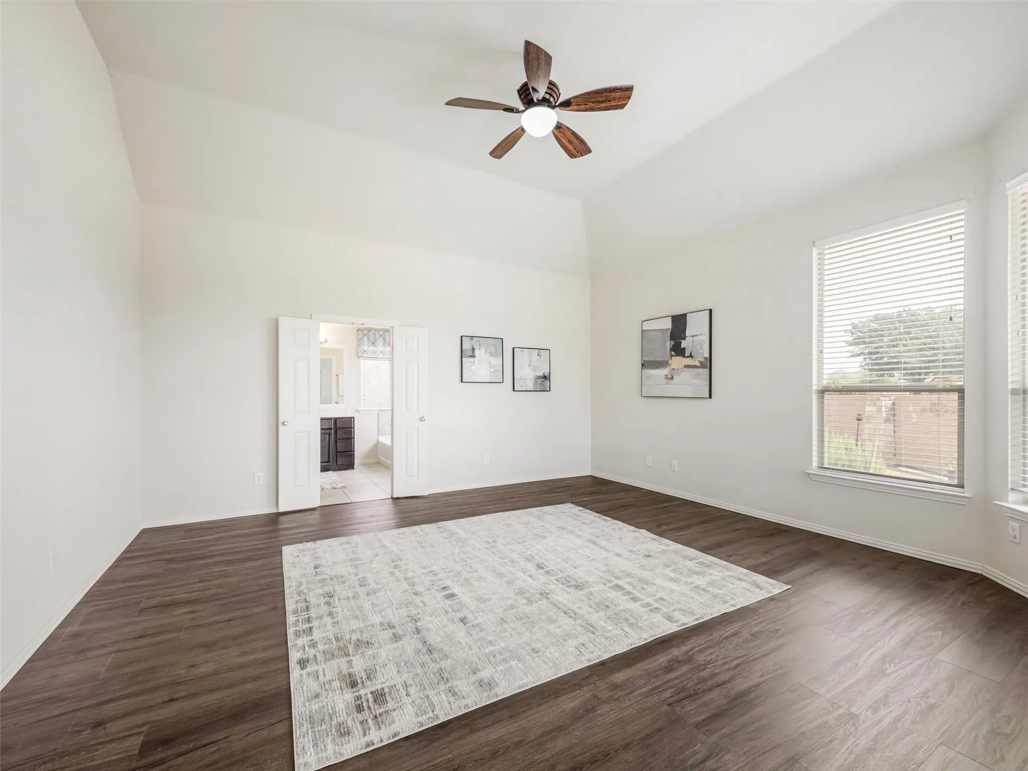 Large windows fill the primary room with natural light. High ceilings and laminate wood flooring create a warm rich feel.