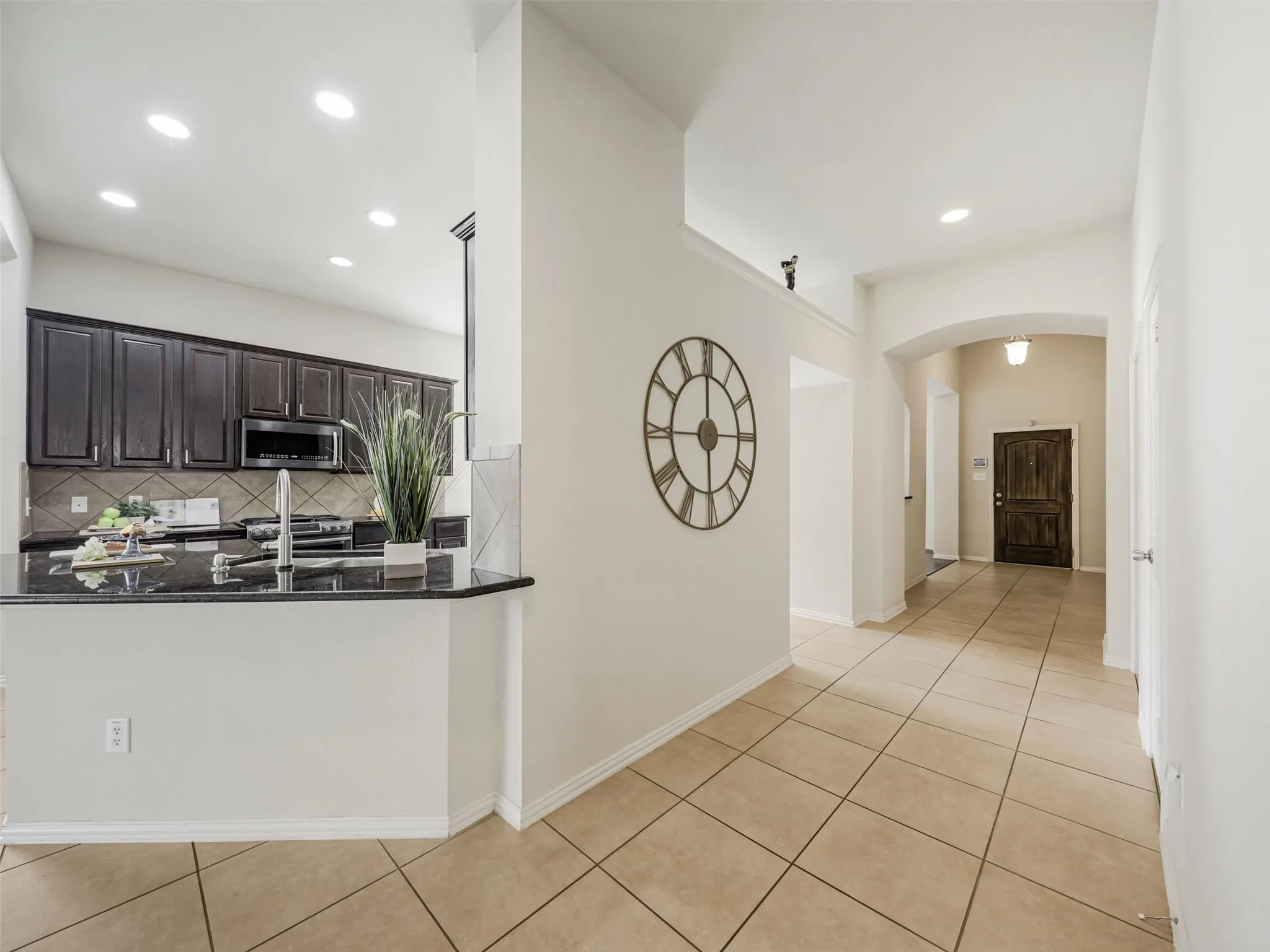 Open layout creates a natural connection between the kitchen and entryway, complemented by tall ceilings, neutral finishes, and tile flooring.