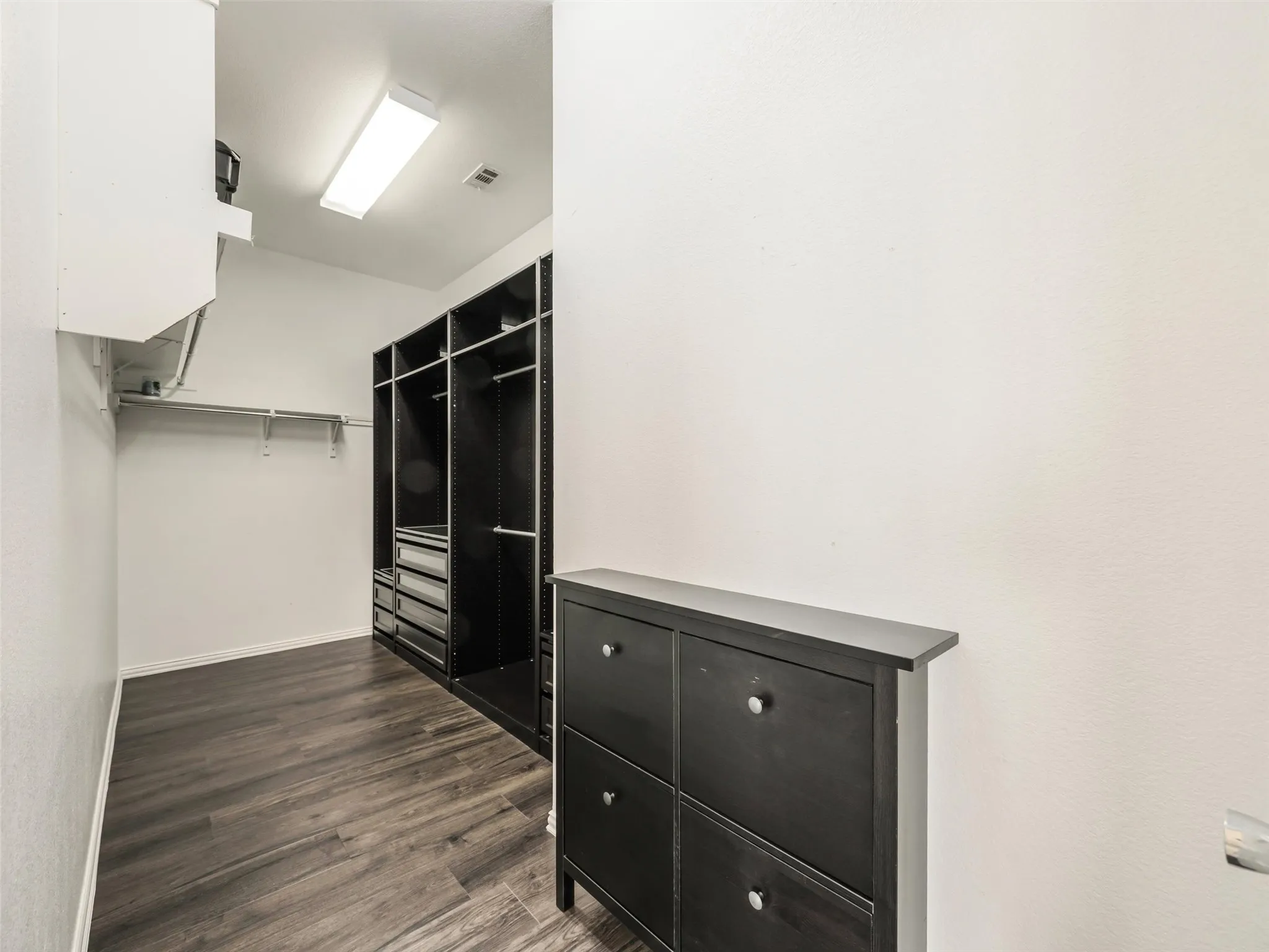 Spacious walk-in closet features built-in shelving, hanging space, drawers, wood-look flooring, and room for additional storage.