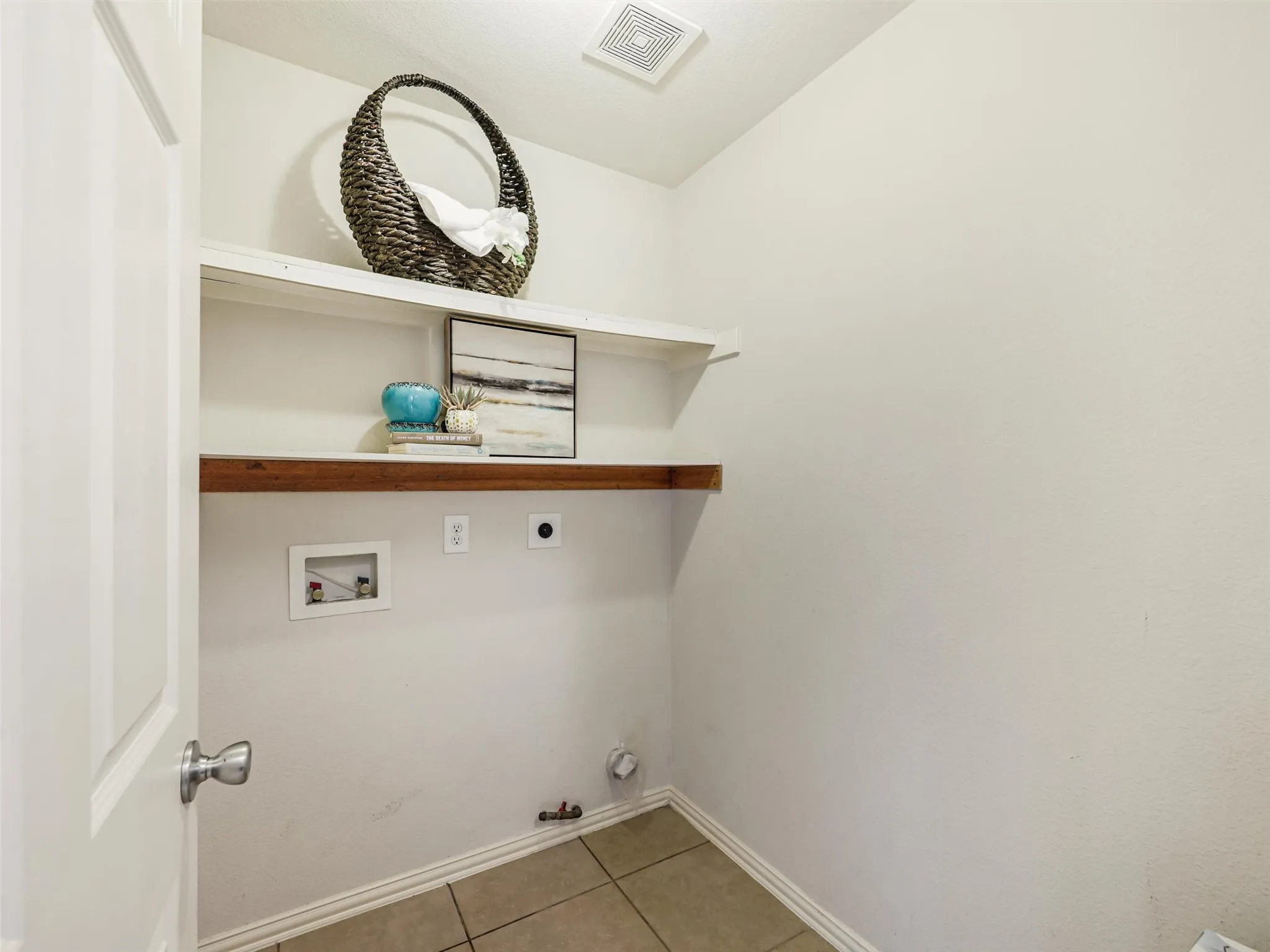 Dedicated utility room offers washer and dryer connections, built-in shelving, tile flooring, and space for laundry essentials.