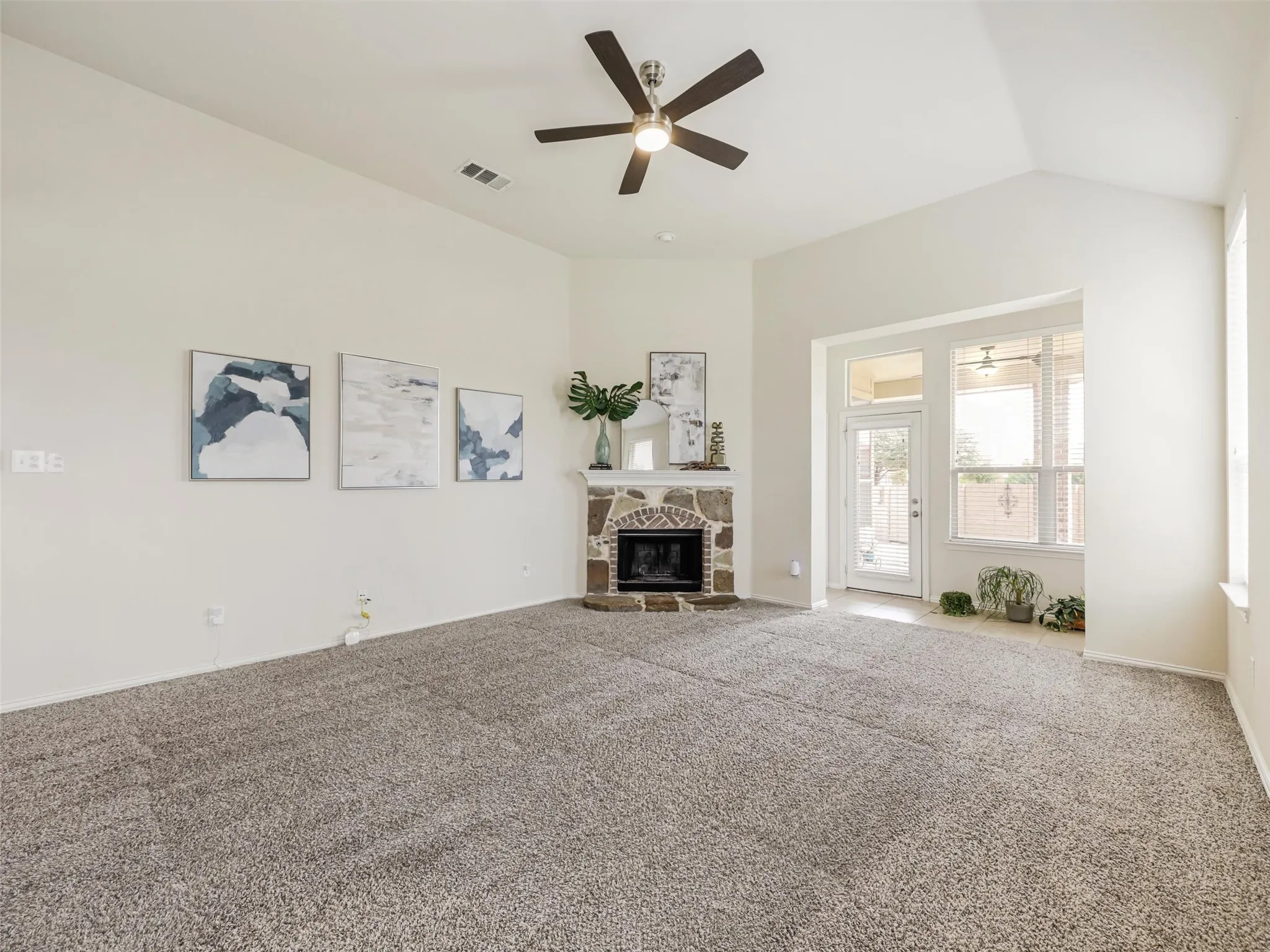 Spacious living room features a vaulted ceiling, plush carpeting, a modern ceiling fan, and a striking stone fireplace.