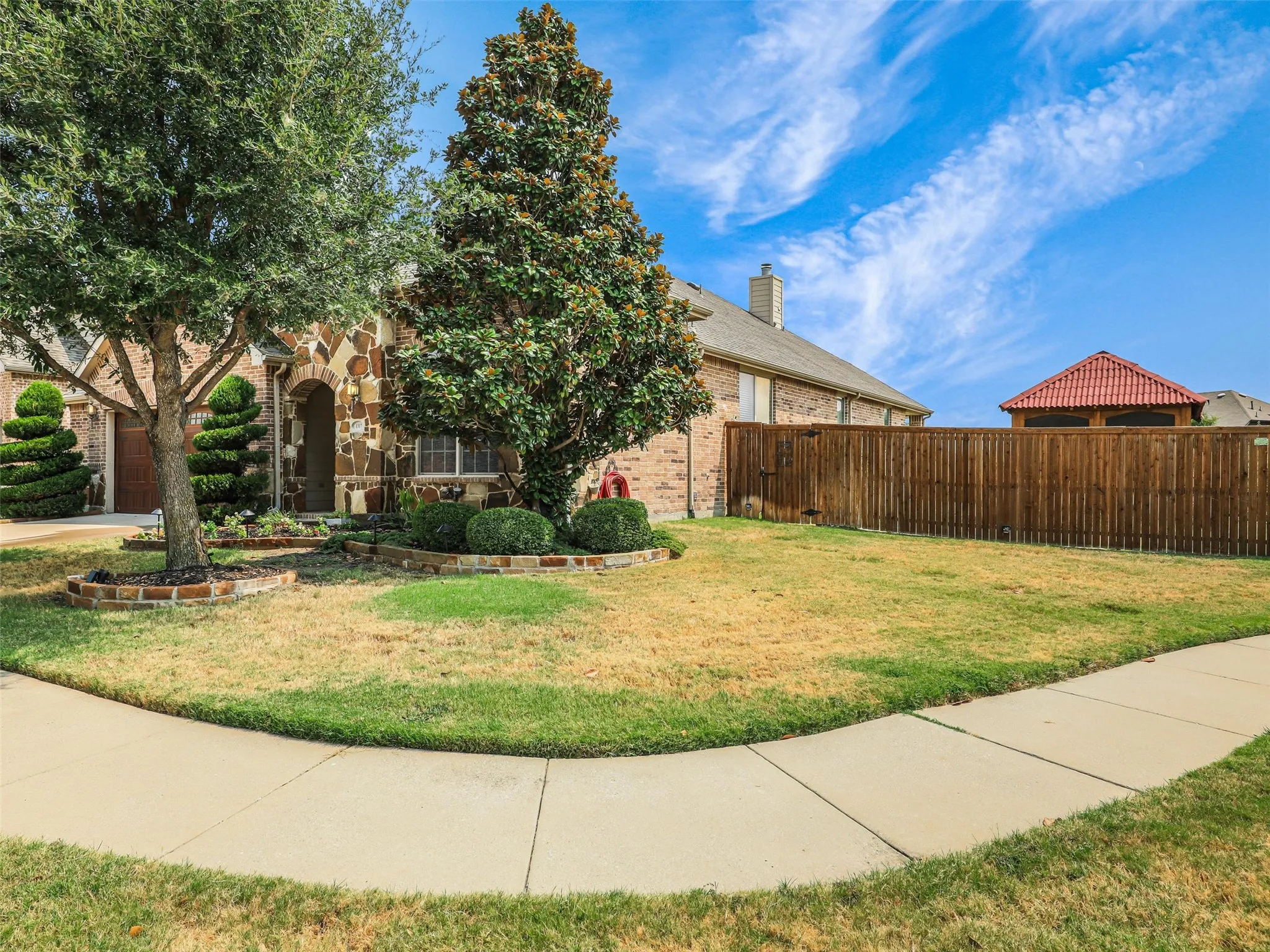 Spacious side yard provides additional outdoor space, complemented by mature trees, landscaping, and a wood privacy fence.