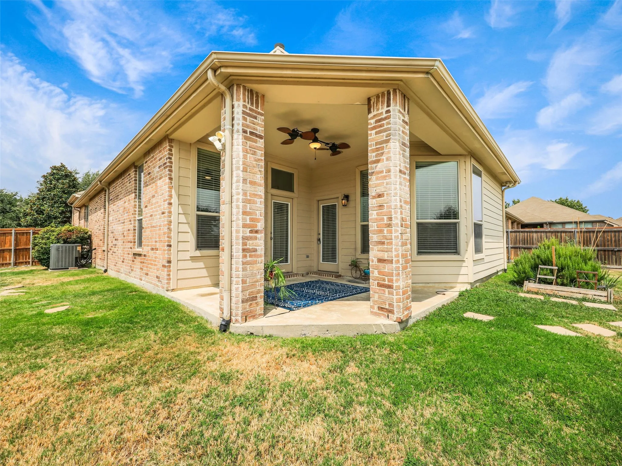 Covered back patio with brick columns, dual ceiling fans, and direct access from the home—an inviting space for relaxing outdoors and a huge yard.