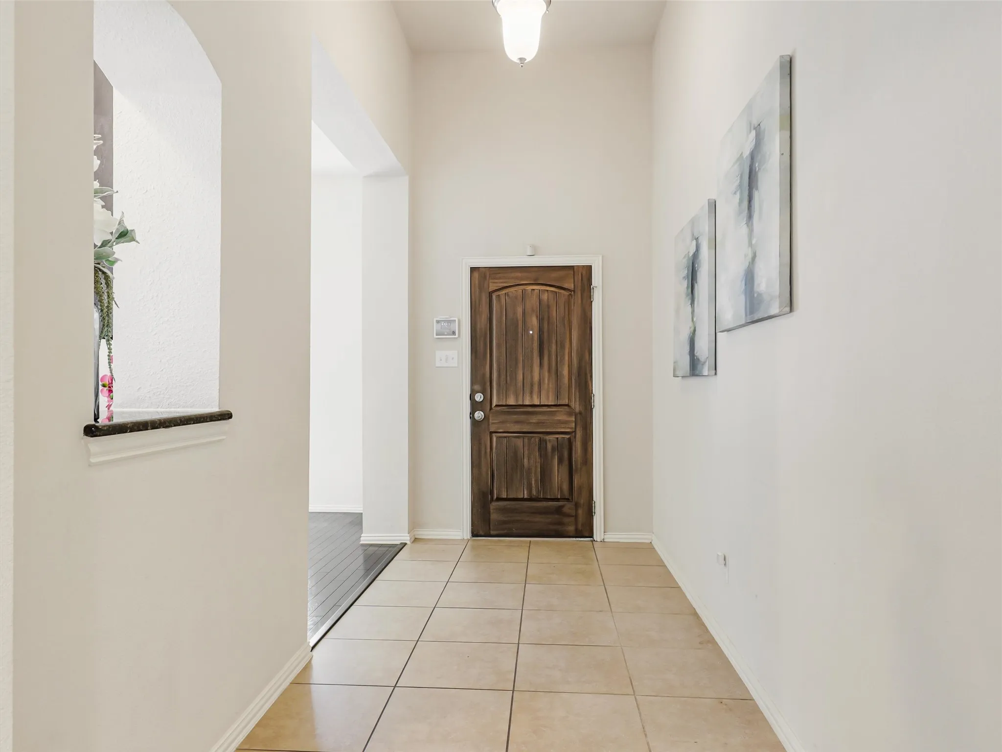 Bright, welcoming foyer with tall ceilings, neutral finishes, tile flooring, and a beautiful wood front door.