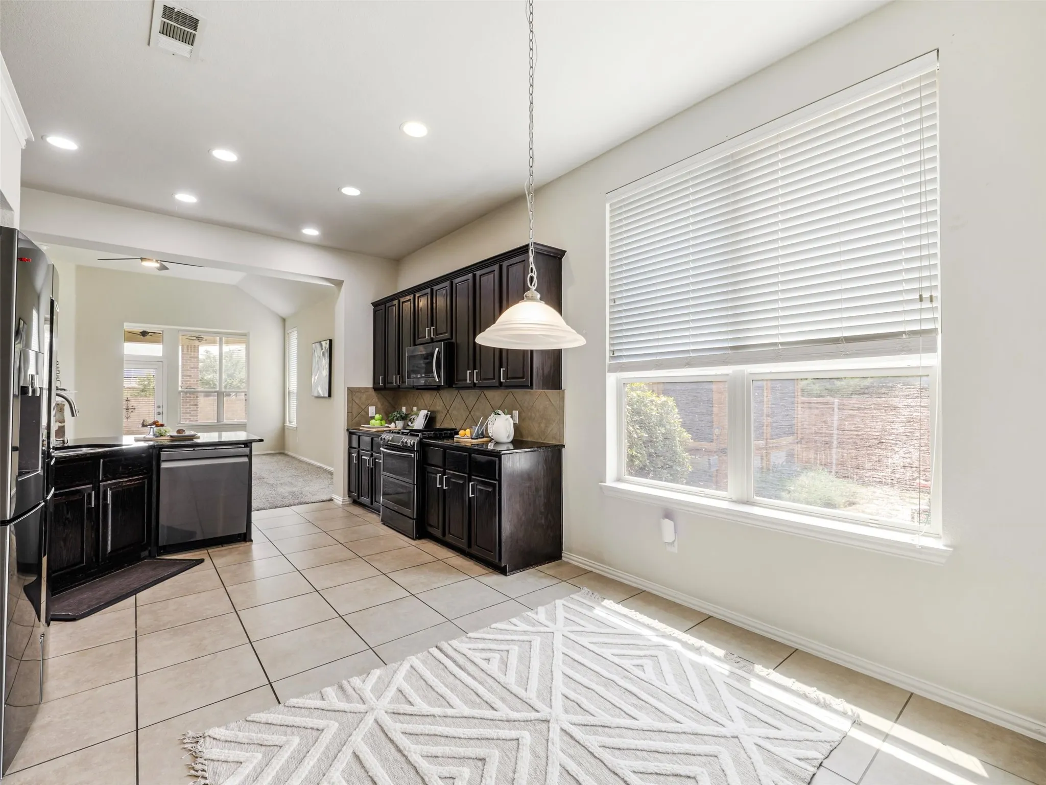 Light-filled kitchen and breakfast area with tall ceilings, recessed lighting, abundant cabinetry, and large windows overlooking the backyard.